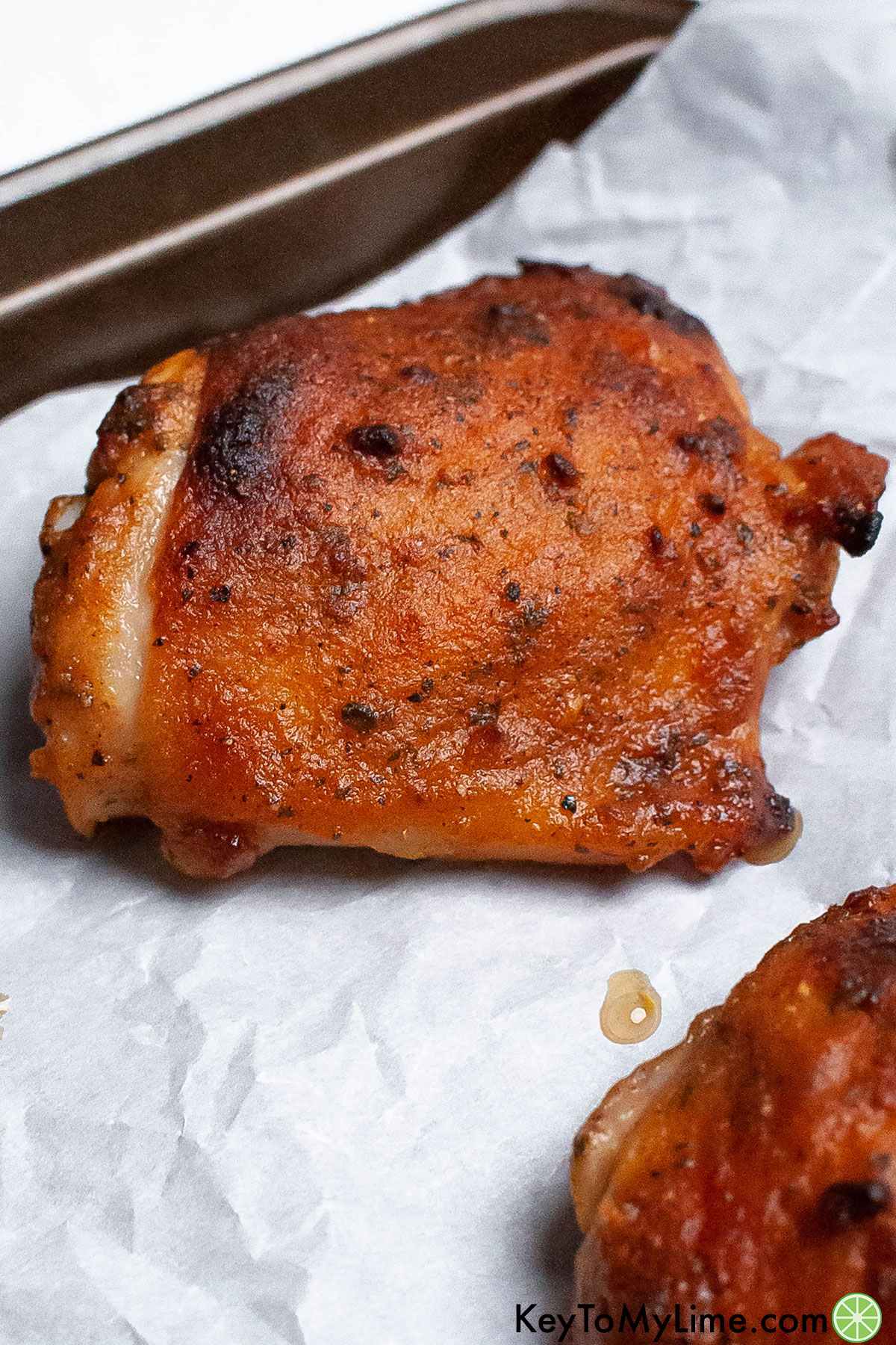 A serving of a couple chicken thighs fully cooked on parchment paper.
