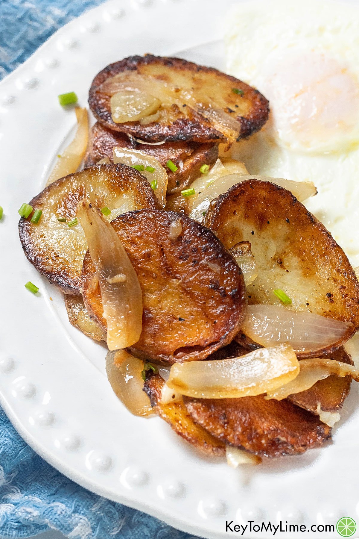 A close up image of fried potatoes and onions with an egg on a white plate.