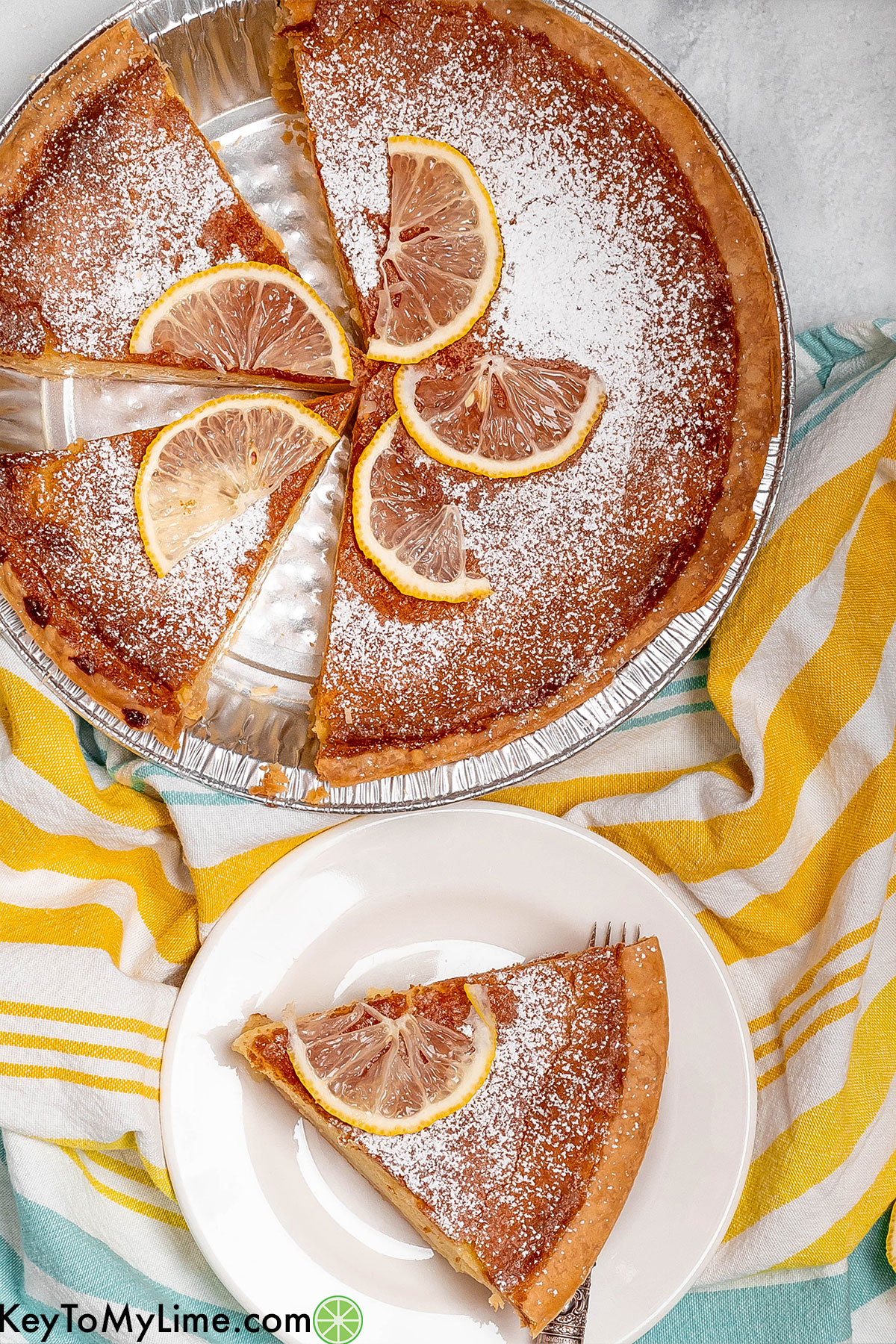 An overhead image of a partially cut pie garnished with lemon wedges and powdered sugar.