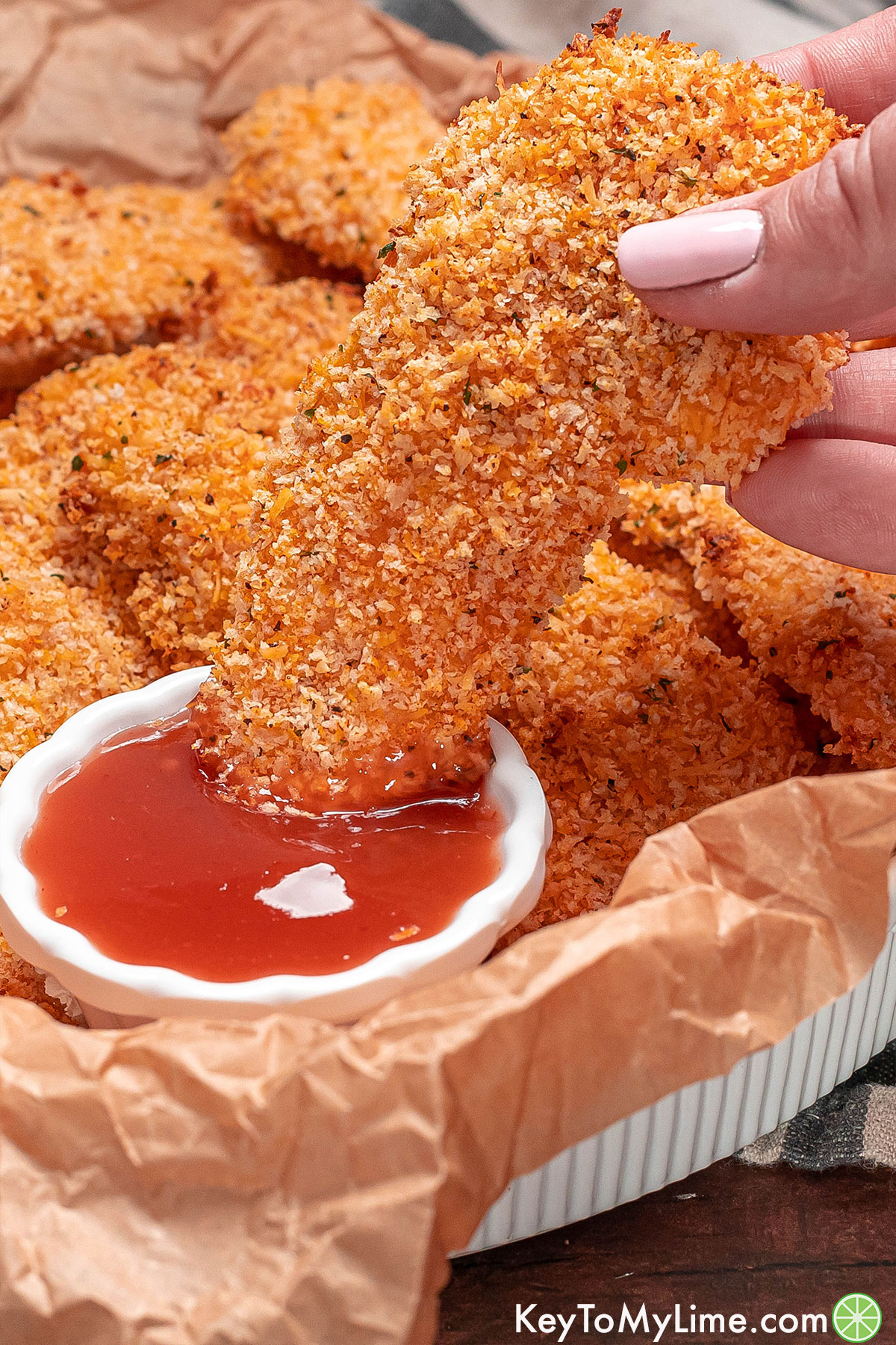 Dipping a chicken tender with panko in a dipping sauce.