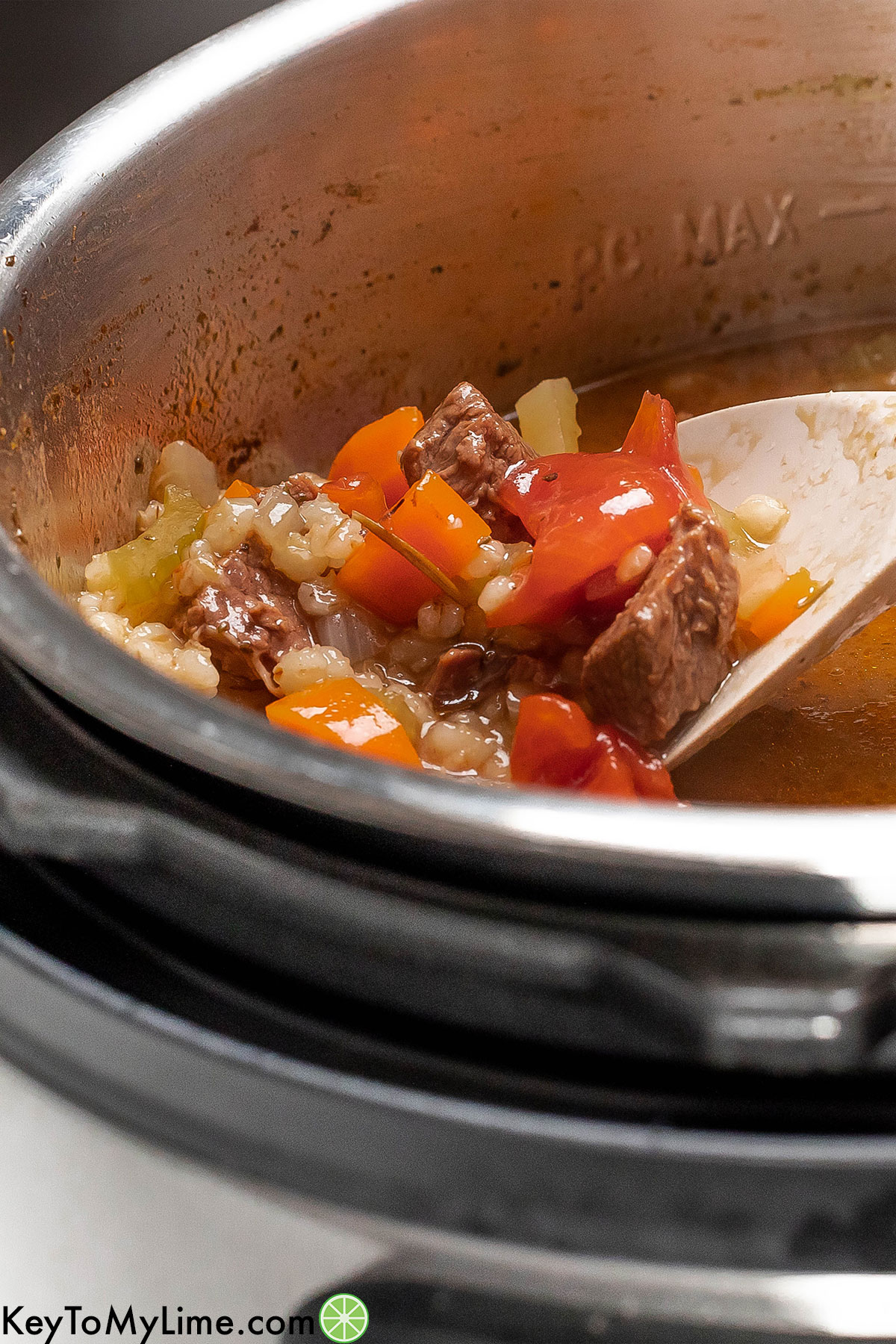 A close up the beef barely soup on a serving spoon inside an instant pot.