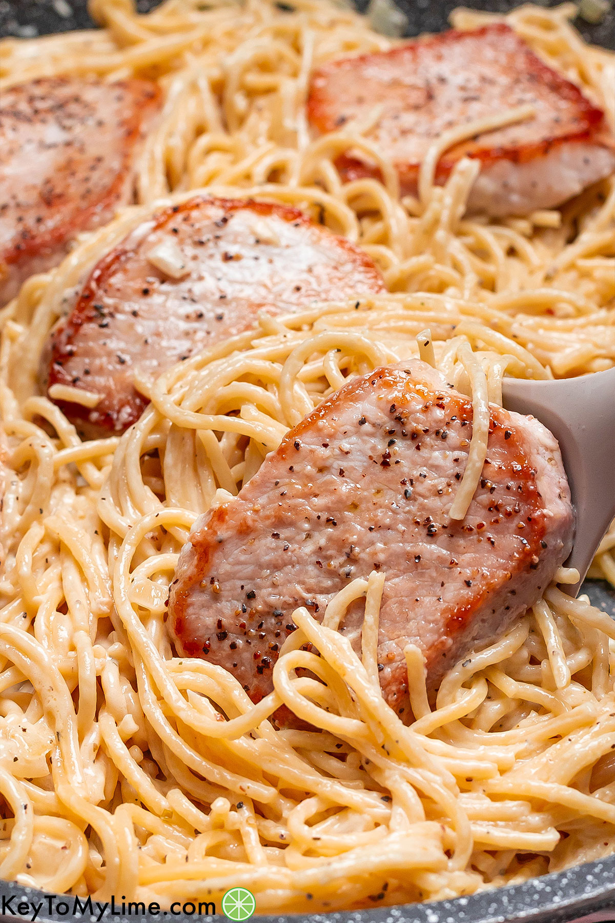 Scooping pork pasta out of a large skillet showing the texture of the thin slices of pork.