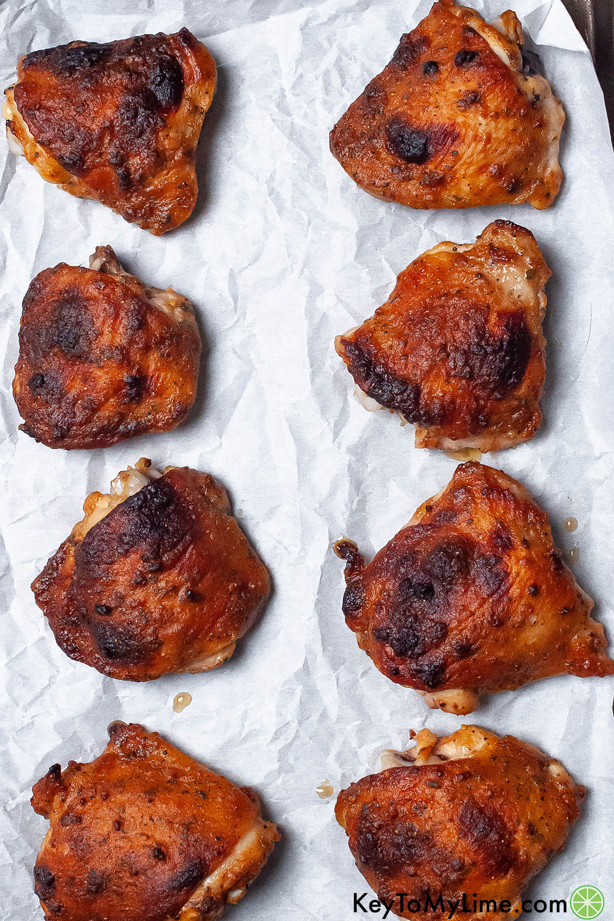A couple of rows of chicken thighs on a parchment paper fresh out of the oven.