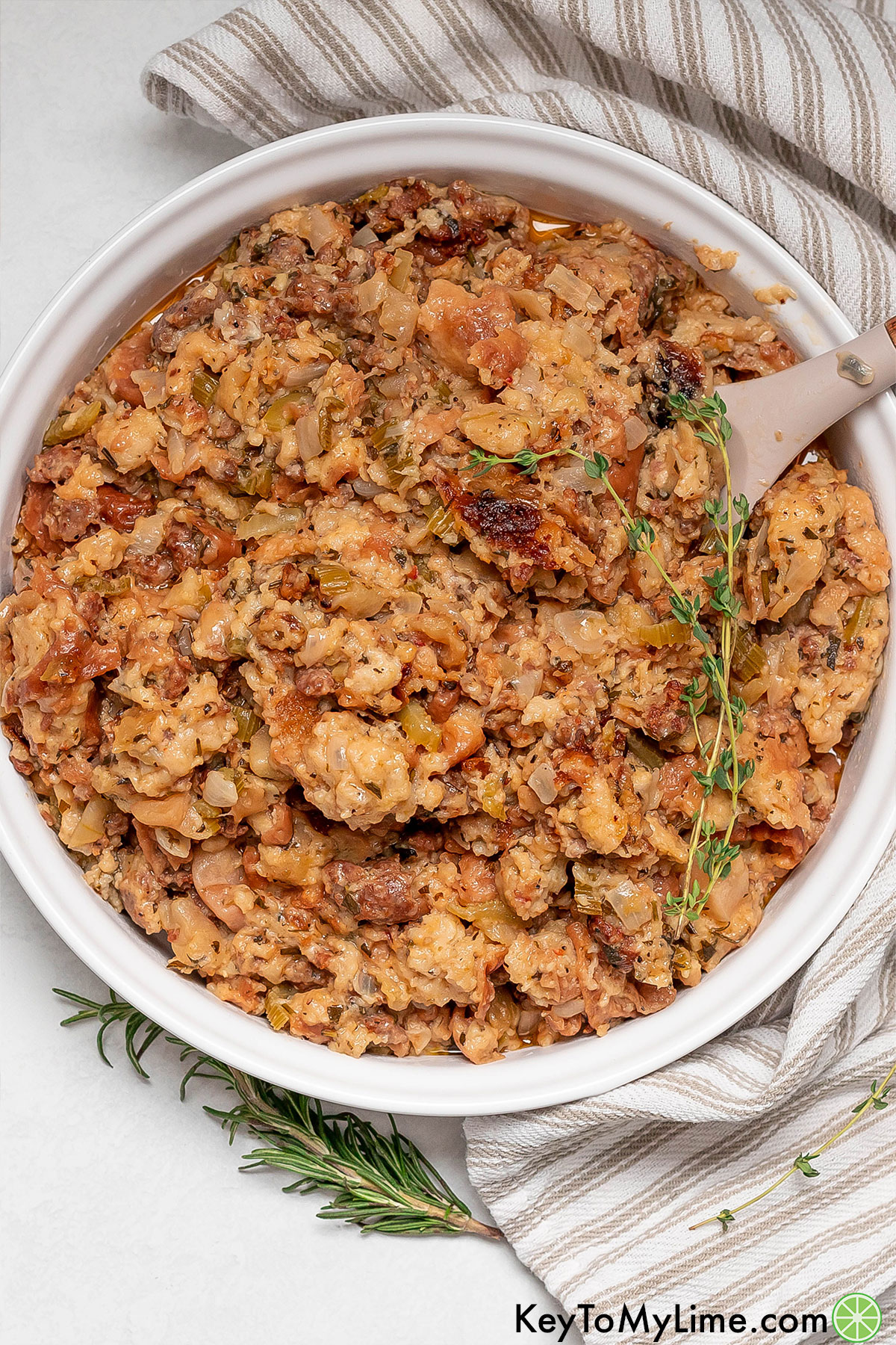 An overhead image of a white serving bowl filled with cooked stuffing over top of a napkin.