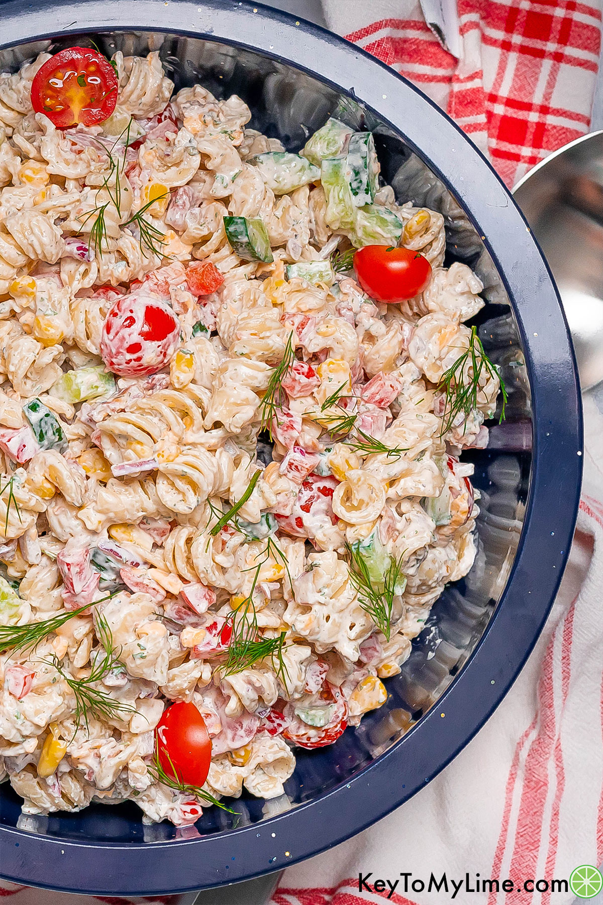 An overhead image of a large serving bowl of pasta salad with cherry tomatoes and cucumber throughout.