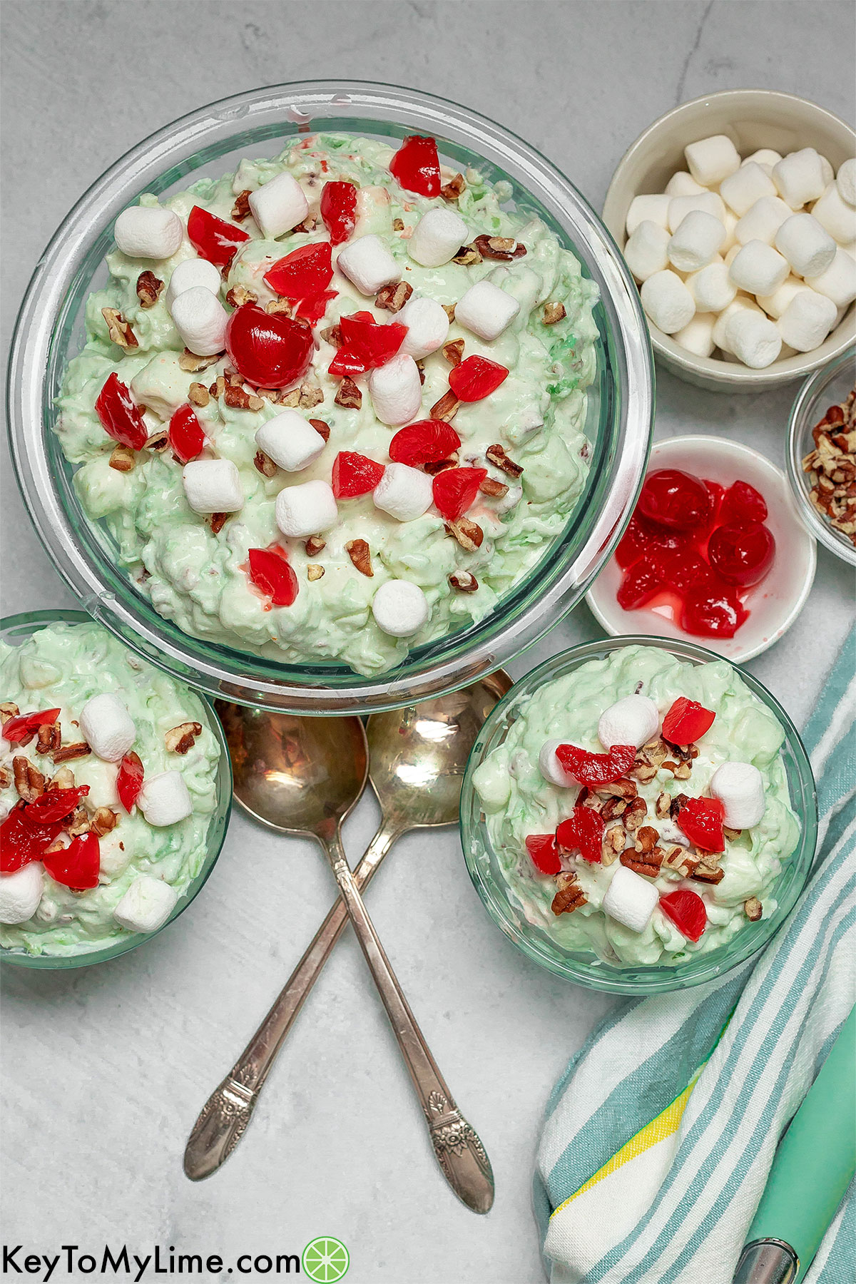 An overhead image of a scene of multiple bowls filled with watergate salad next to a couple of garnish bowls.