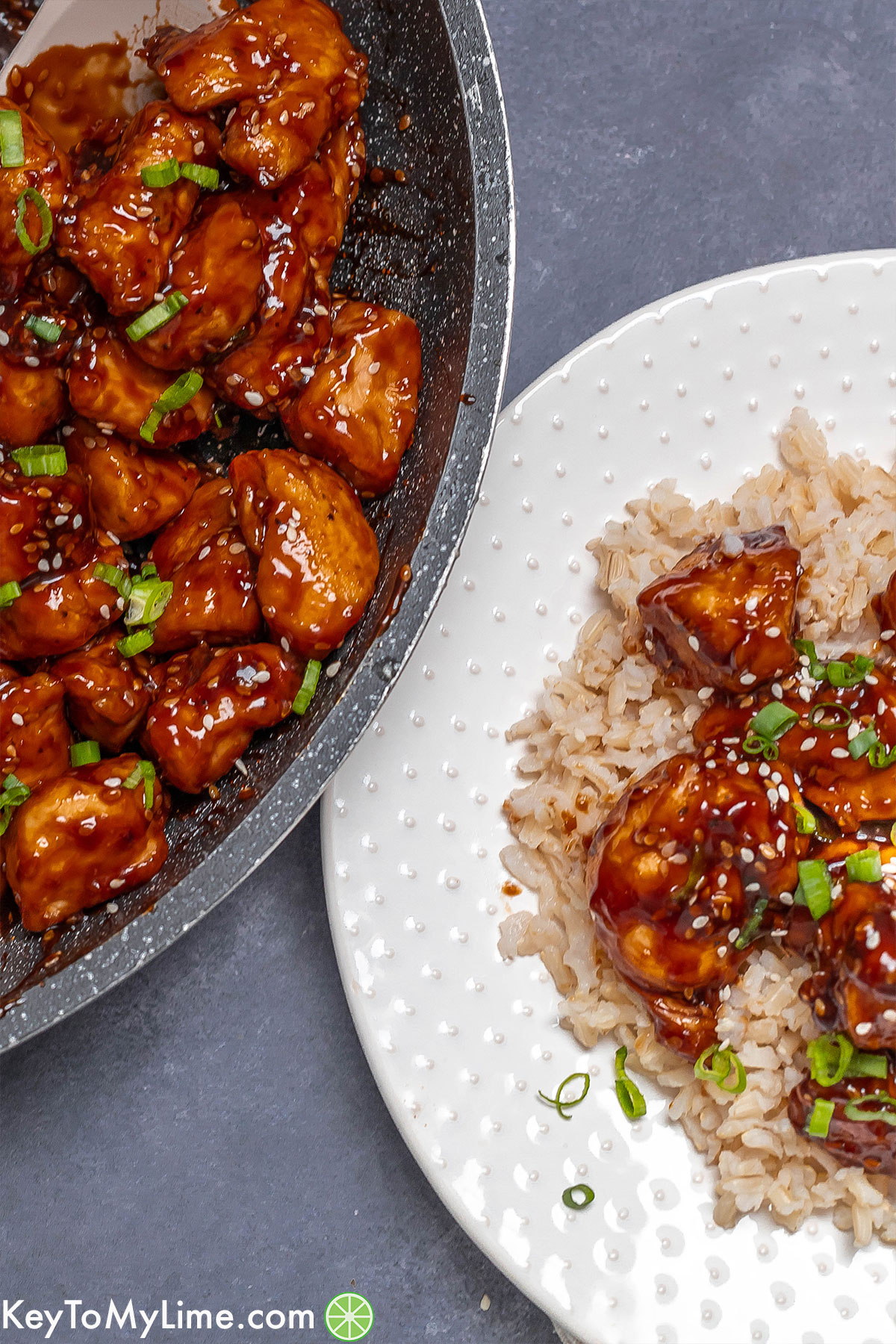 A partial pan and plate full of garnished honey sesame chicken.