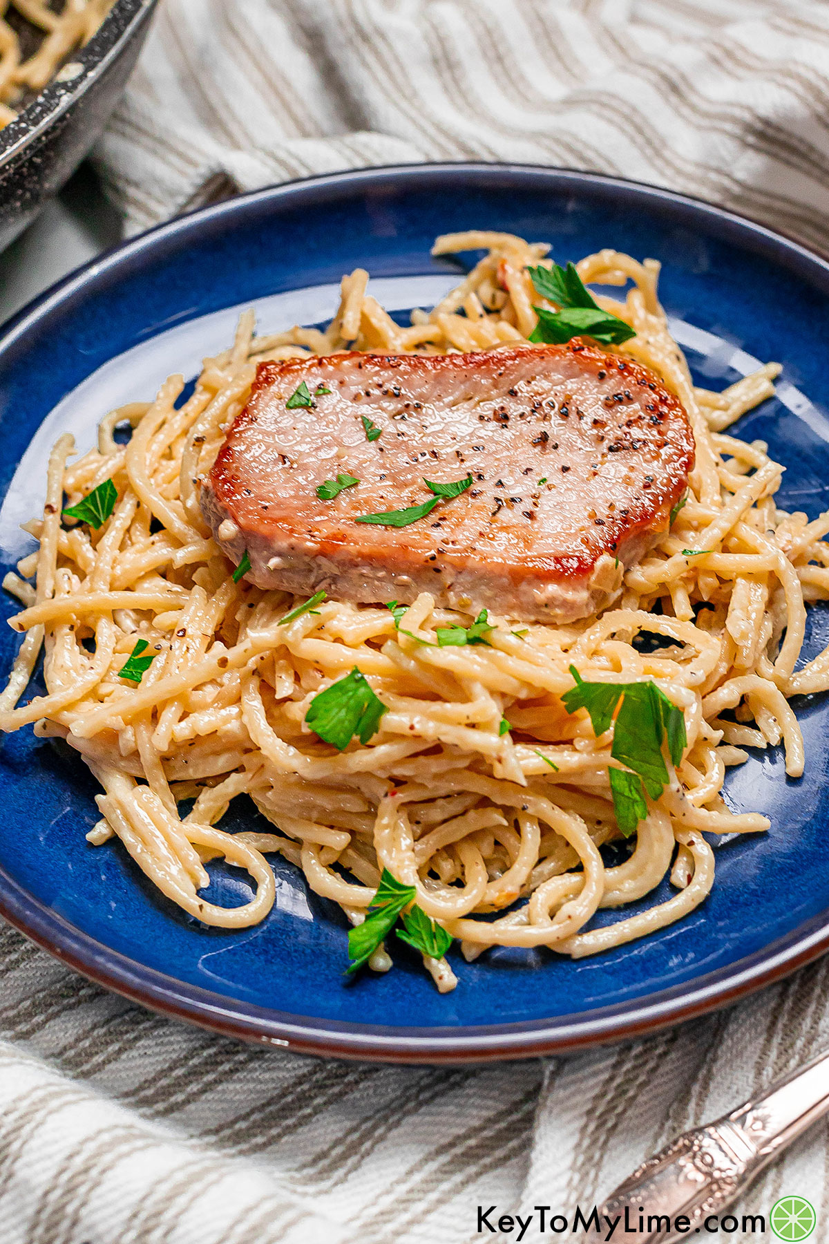 A pile of creamy pasta topped with a juicy tender pork chop slice.