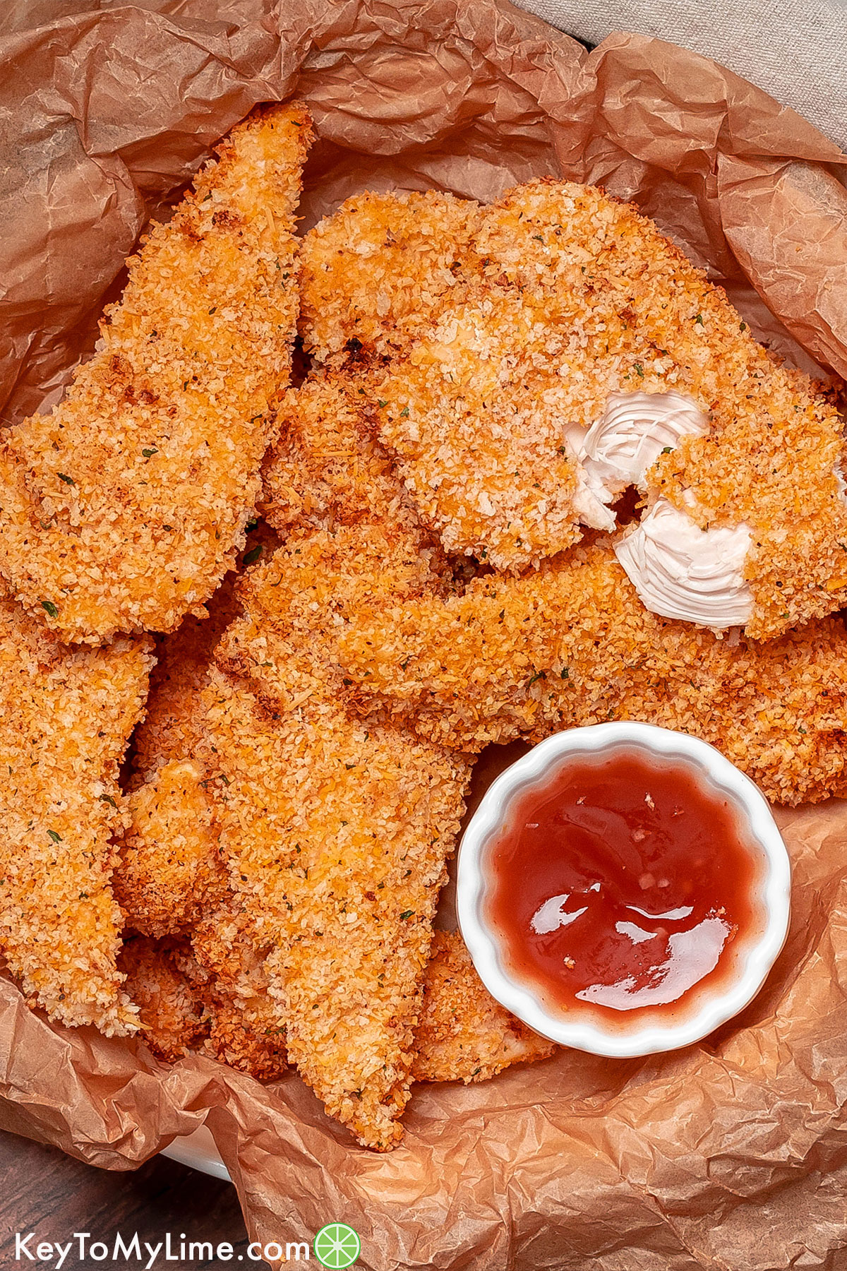 A pile of panko chicken tenders with a split tender on top showing the juicy inside texture.