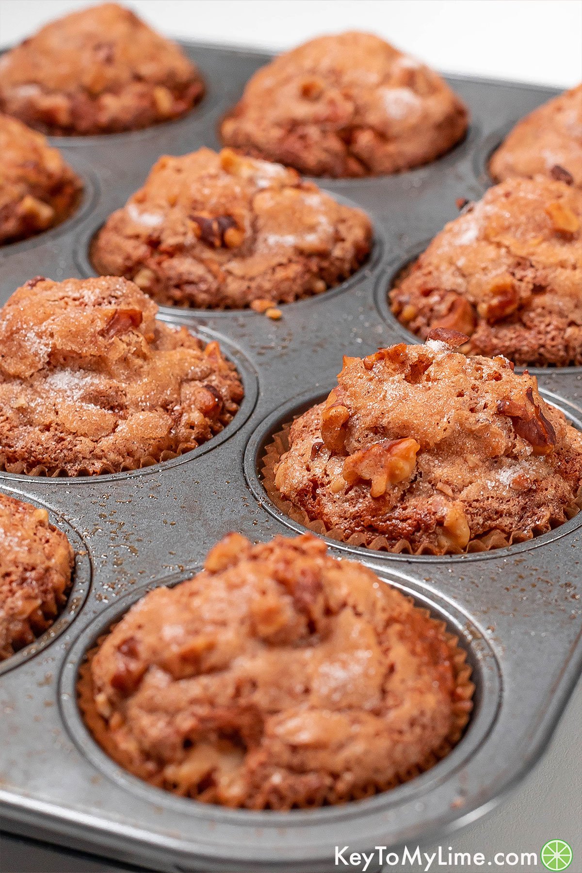 Side shot of banana muffins in a baking tin showing the sugary crunchy topping.