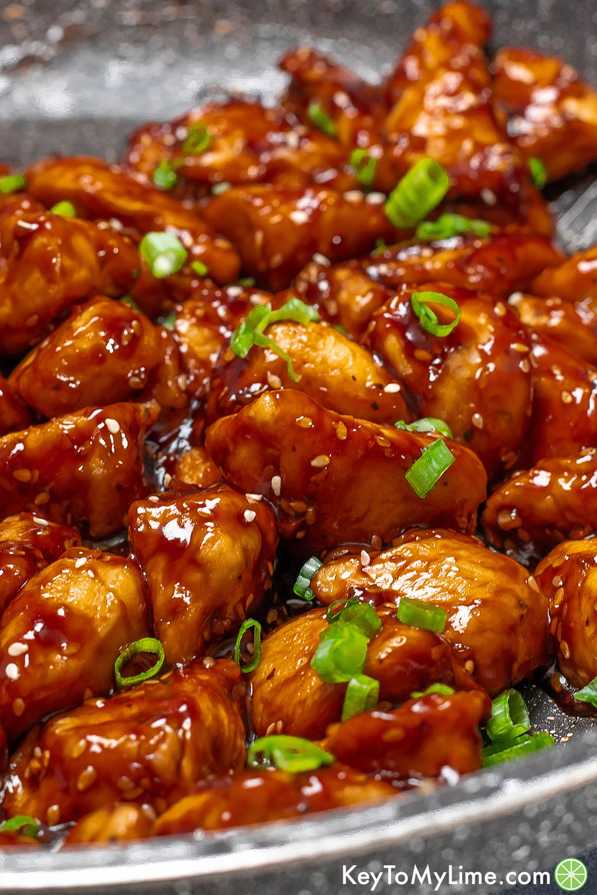 A close up of saucy honey coated chicken garnished with fresh green onions.
