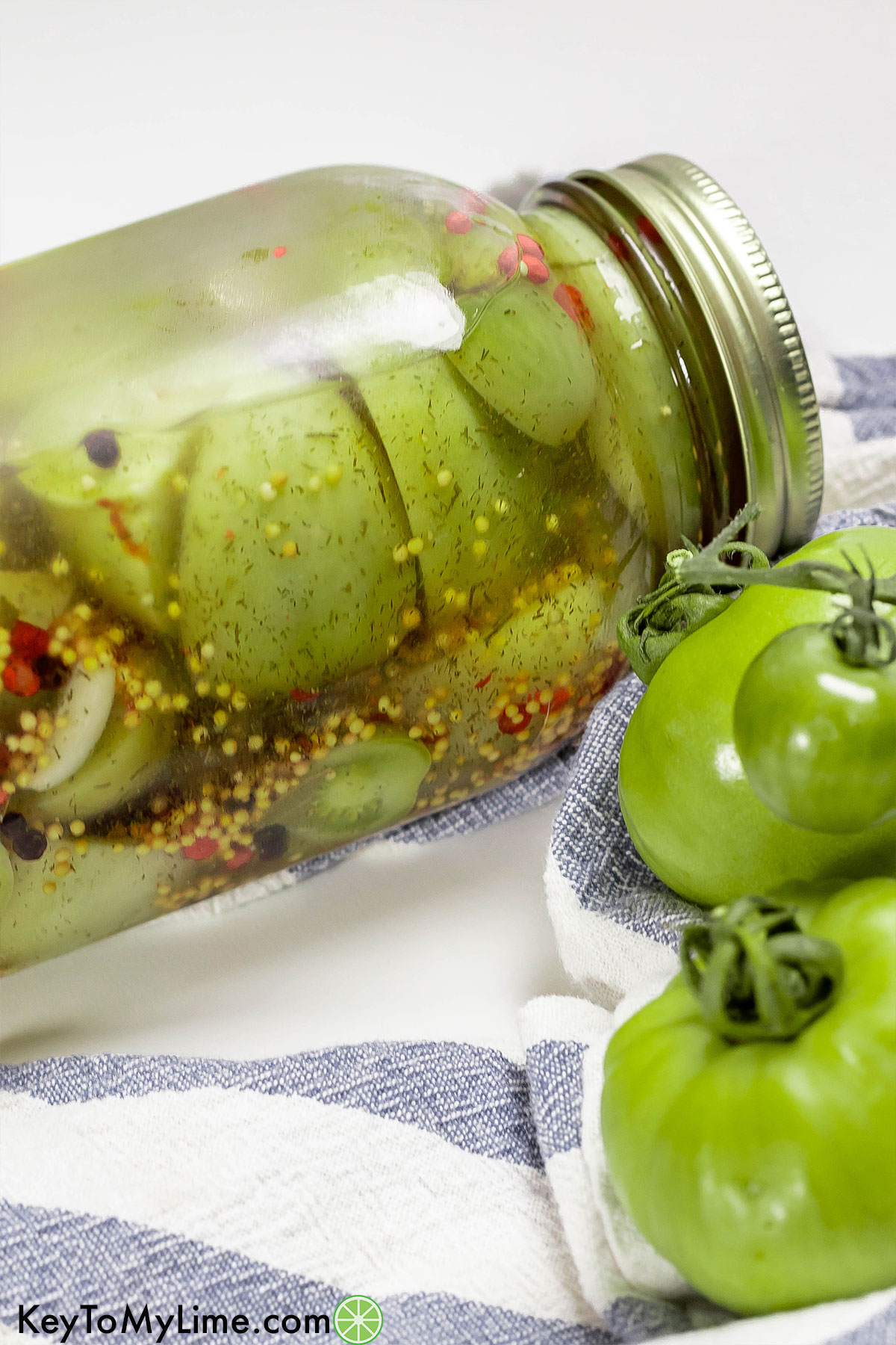 A close up of a jar of pickled tomatoes showing the peppercorn mixture.