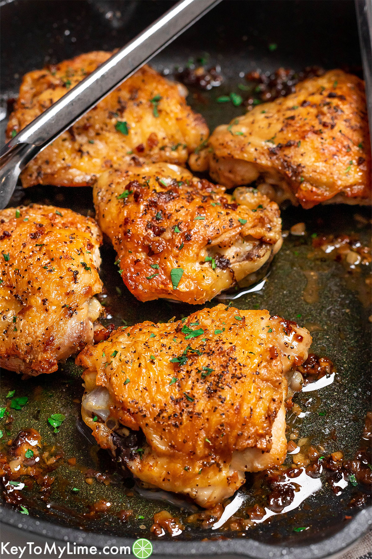 A close up image of crispy chicken thighs with fresh parsley garnished in a skillet.
