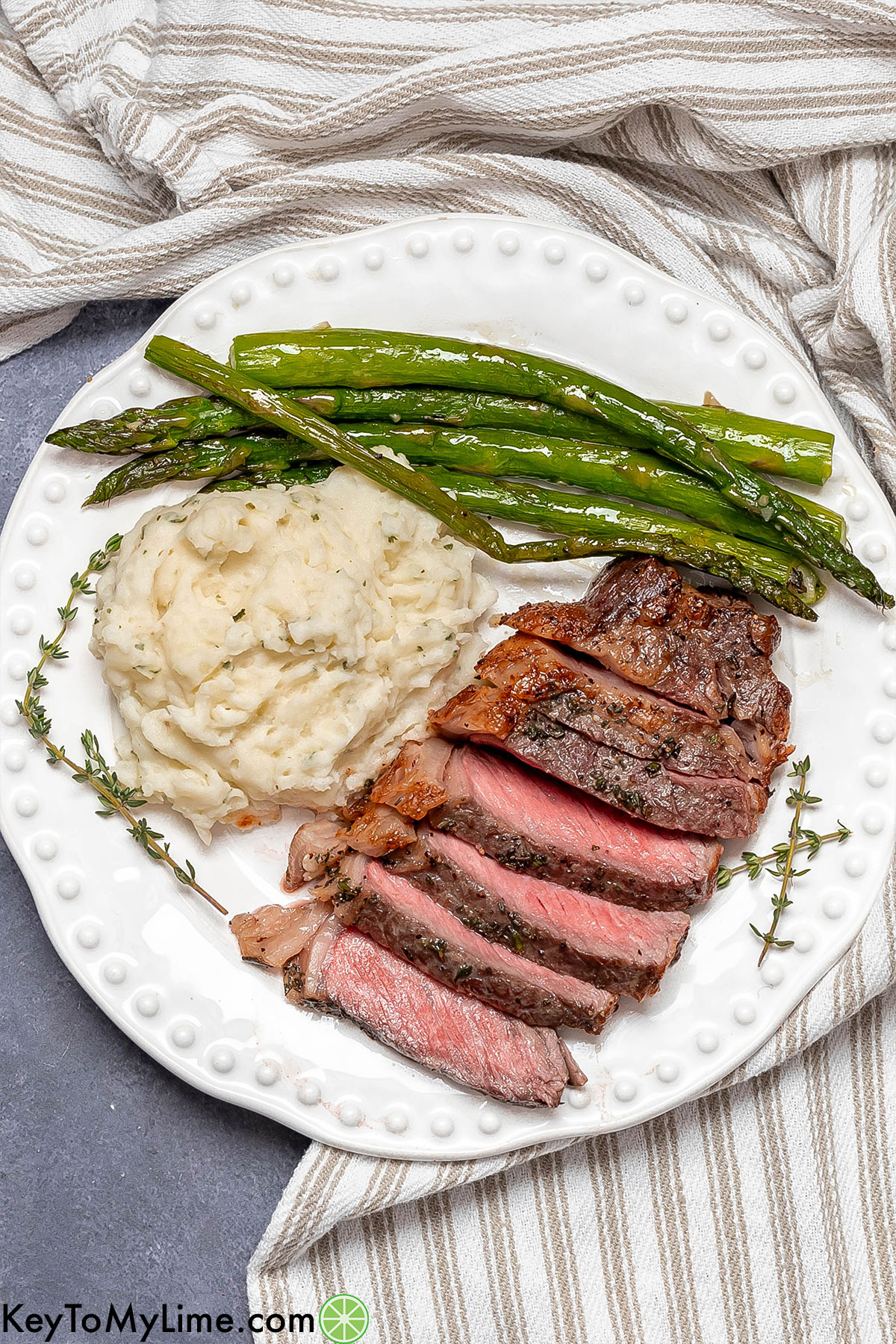 Juicy tender sliced steak plated with freshly cooked asparagus and potatoes with a napkin in the background.