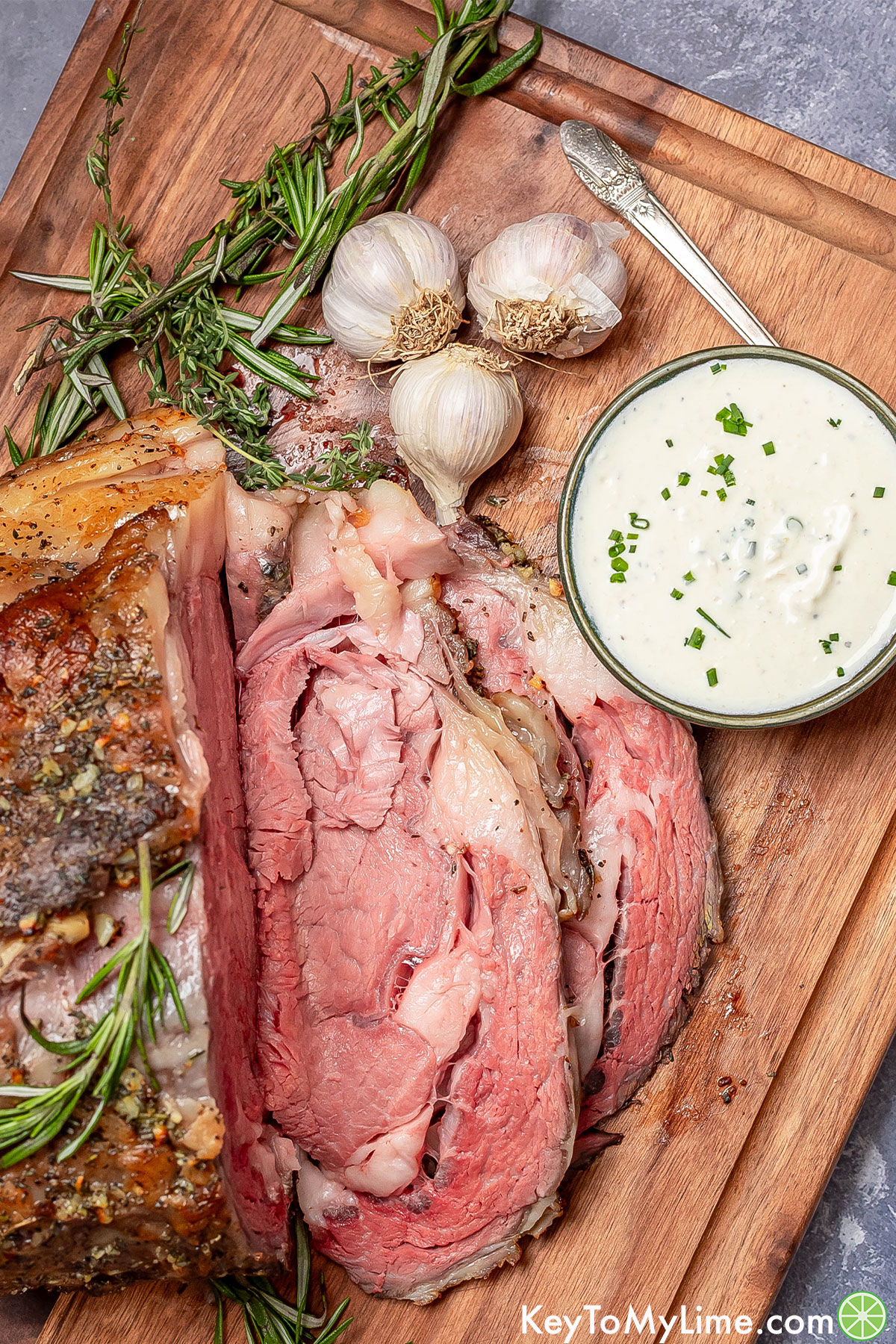 An overhead image of a sliced prime rib roast next to small bowl of garnished horseradish sauce on a cutting board.