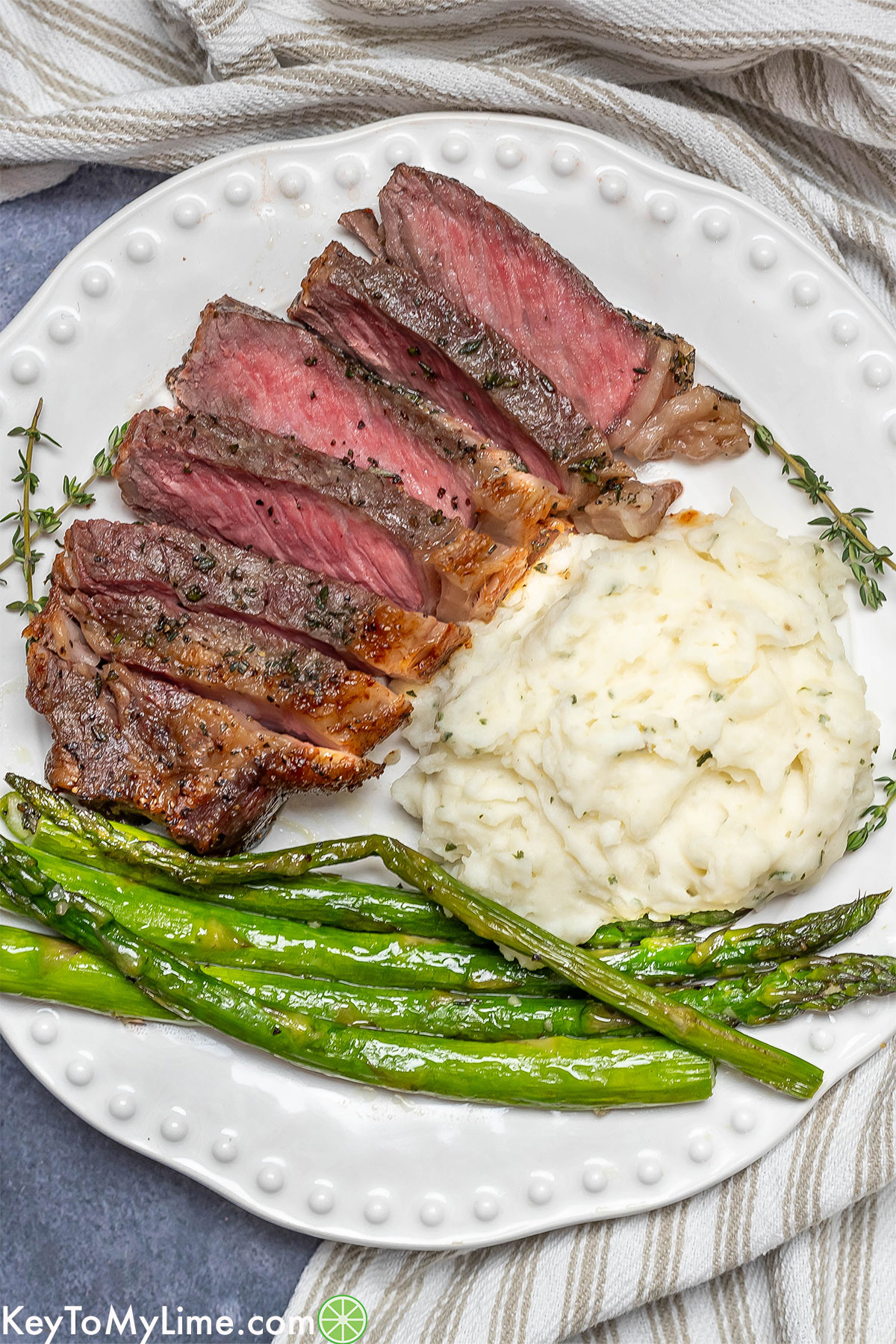 A white dinner plate with freshly sliced steak, mashed potatoes, and asparagus.