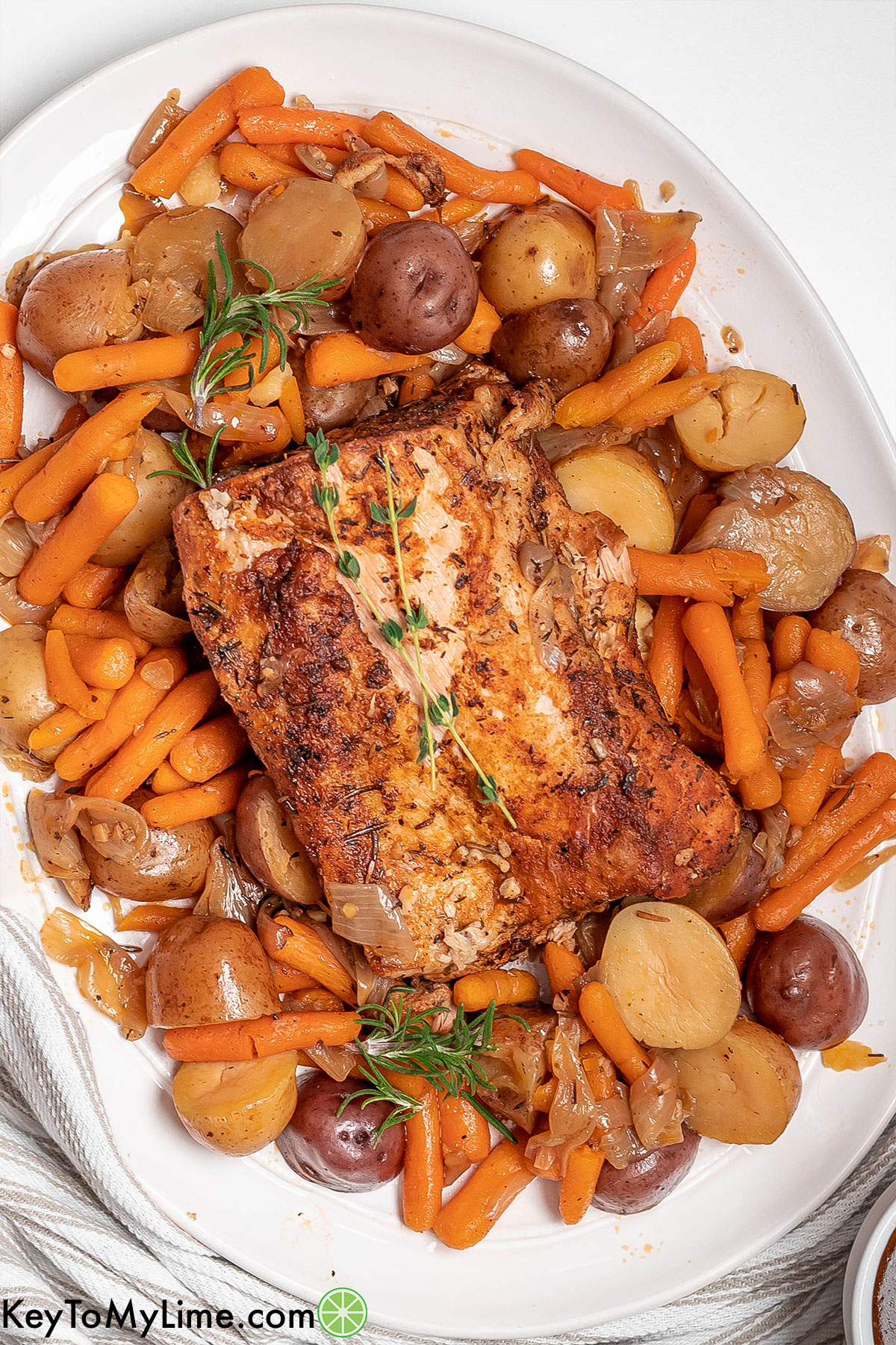 An overhead image of a fully cooked pork loin garnished with fresh rosemary and vegetables throughout.