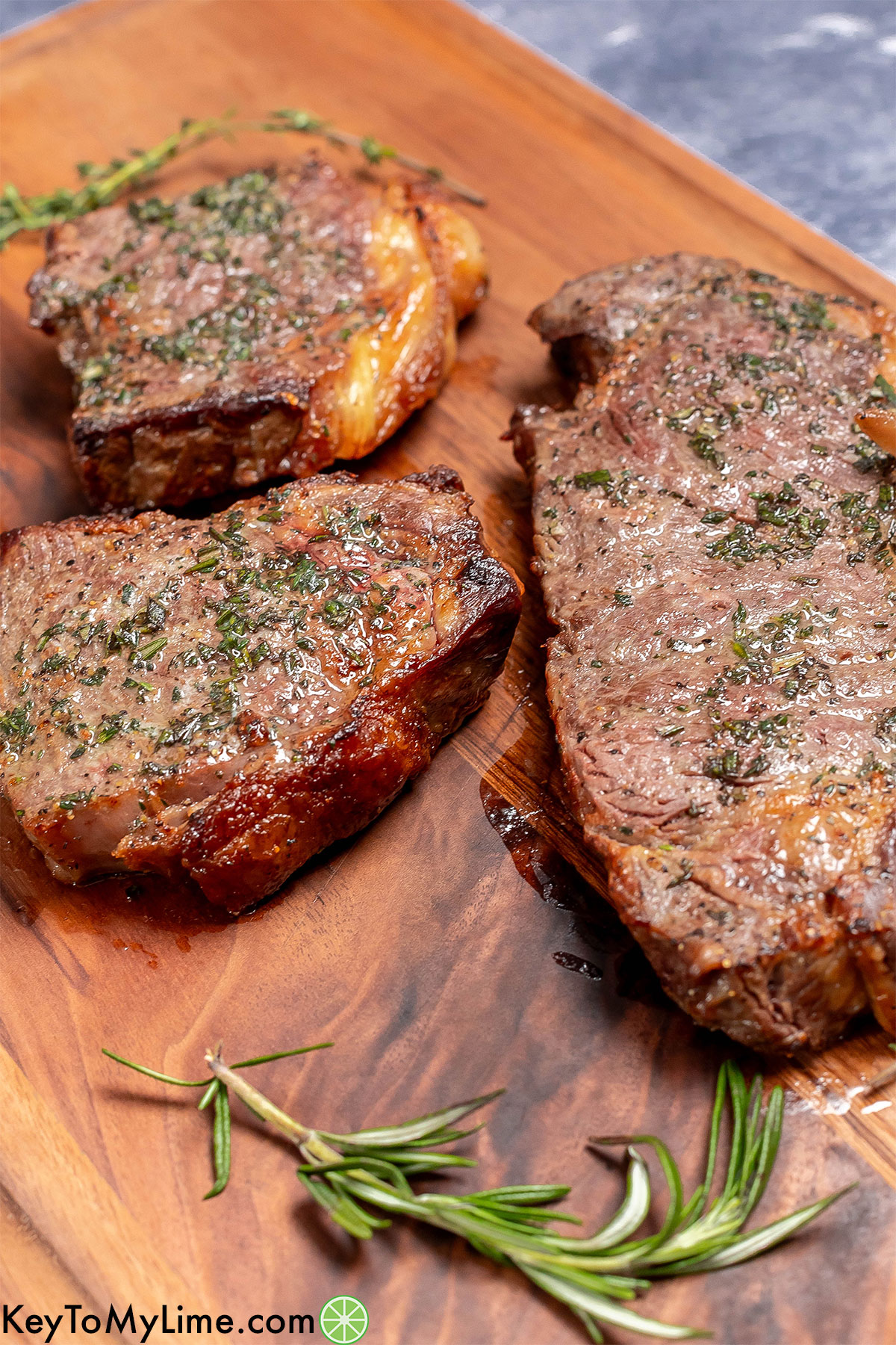 Steaks resting on a wood cutting board with fresh garlic herb butter on top.
