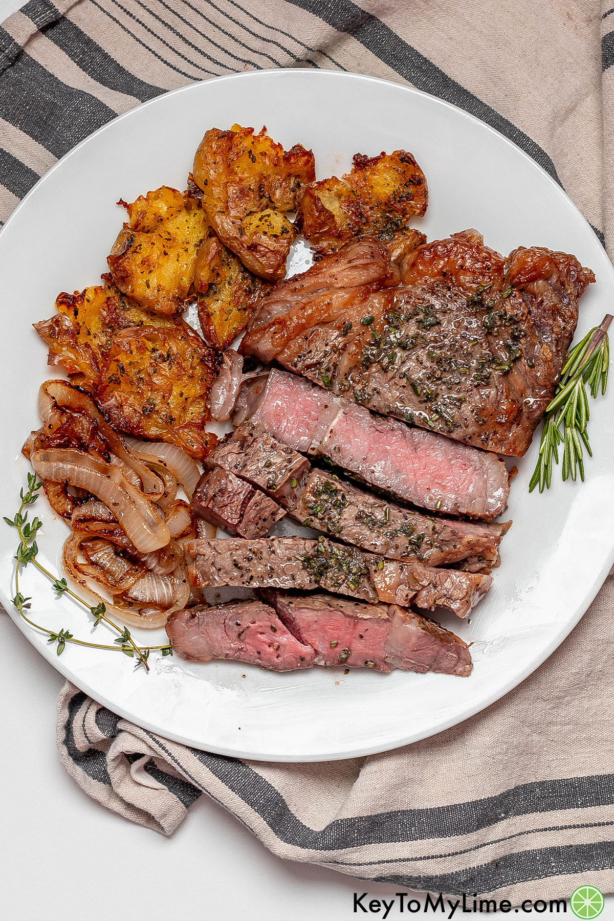 An overhead image of a serving of ribeye steak next to potatoes and onions.