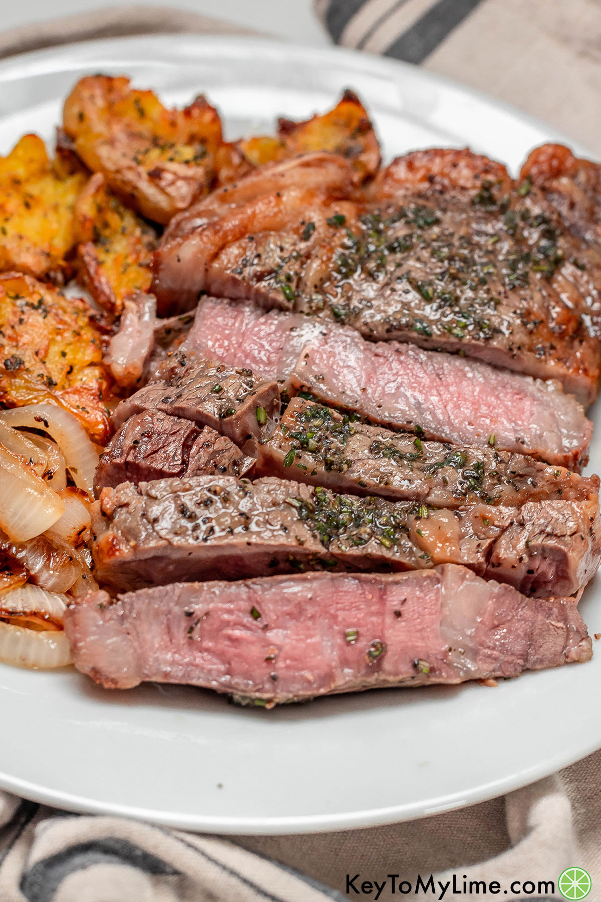 A side image of a sliced ribeye covered in herb butter next to a serving of potatoes.