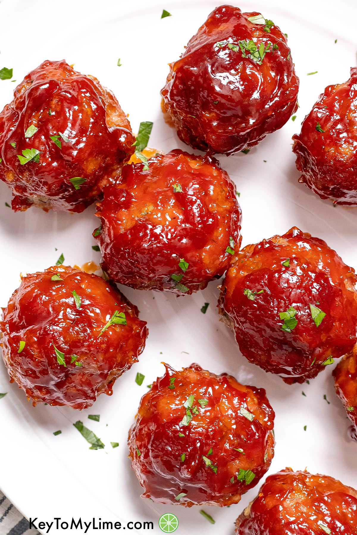 A close up image of a bunch of ham balls on a large white platter freshly garnished with parsley.