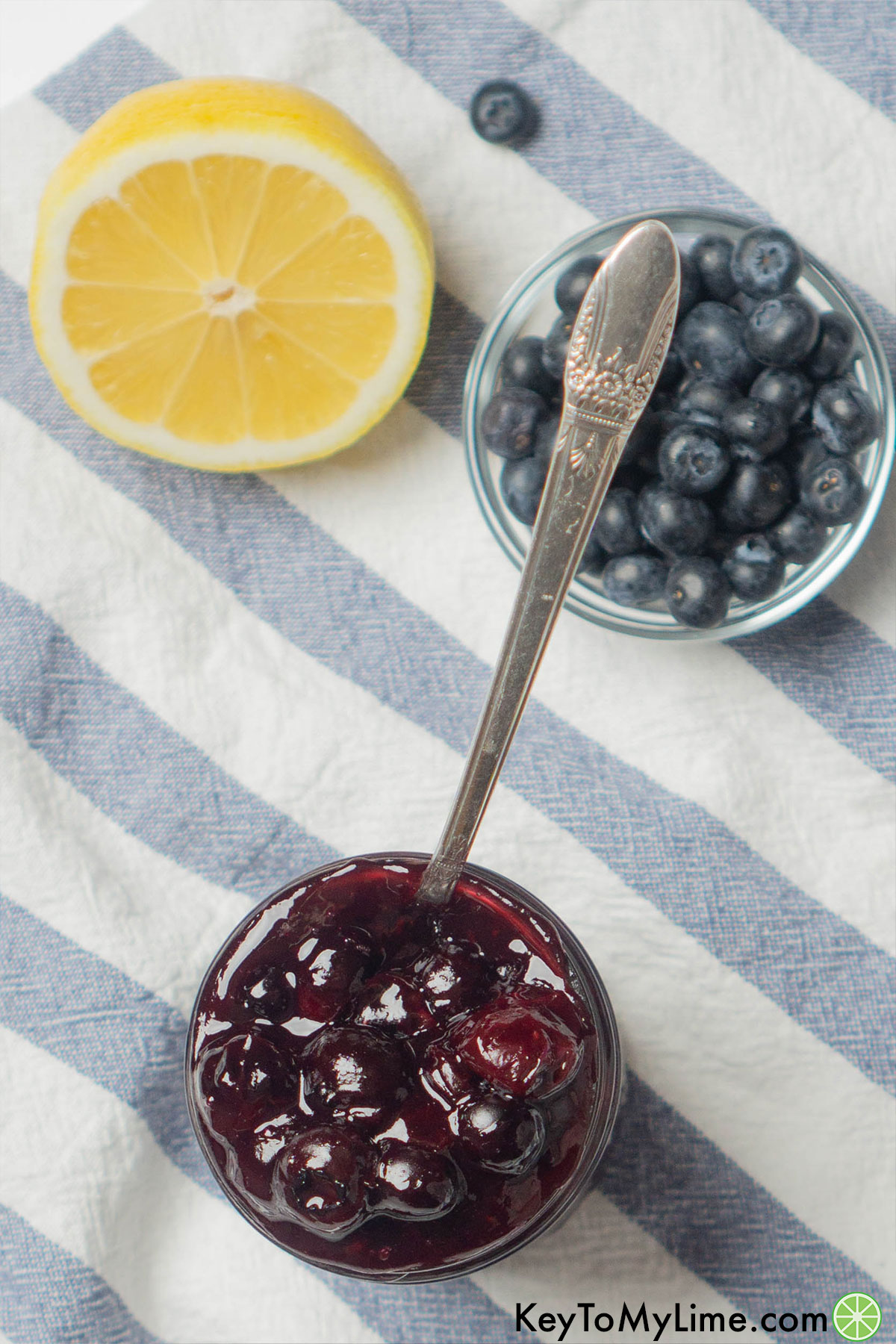Delicious blueberry filling in a jar next to a small bowl of blueberries and half a lemon.
