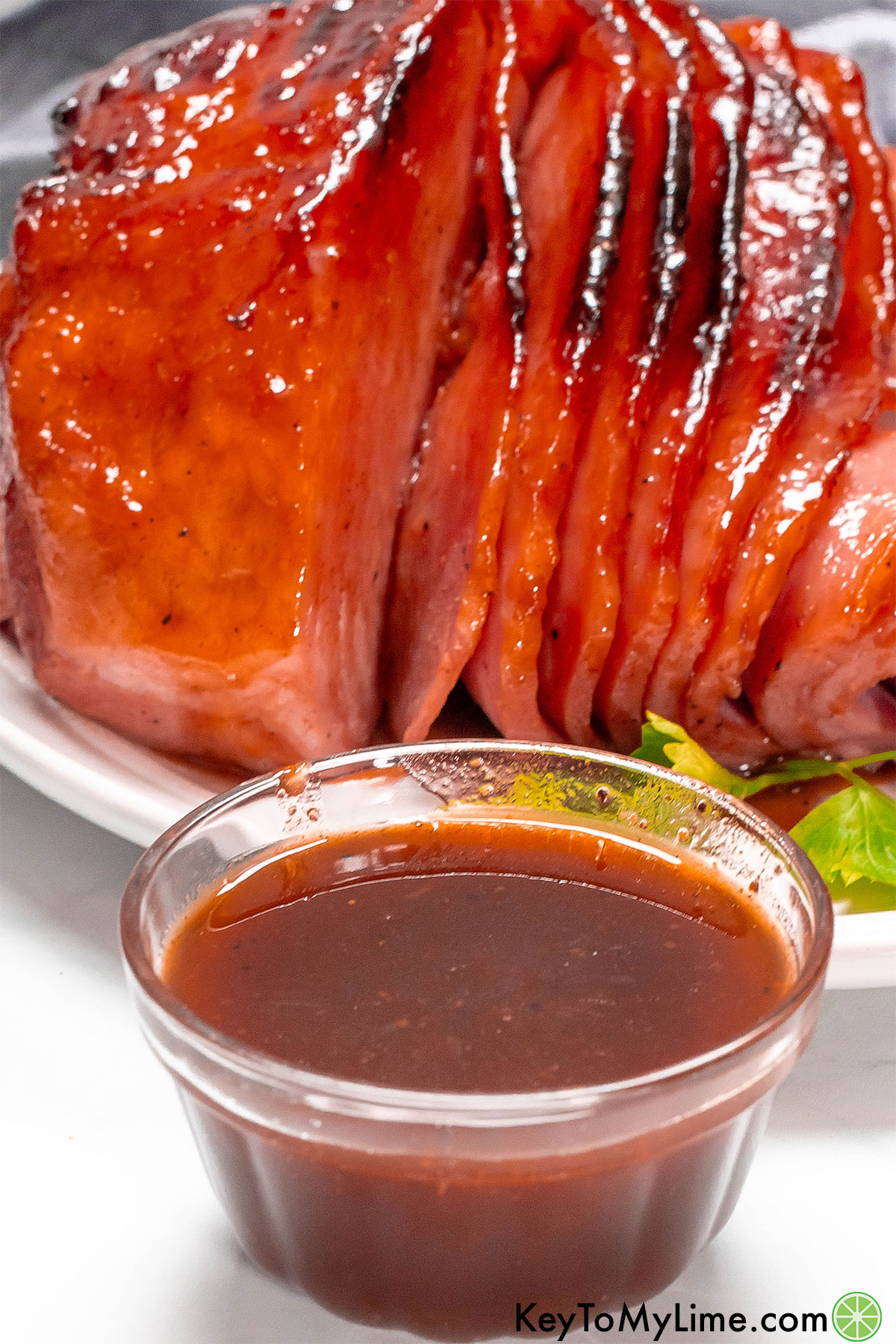 A close up image of a small bowl of pineapple ham glaze with a spiral ham in the background.
