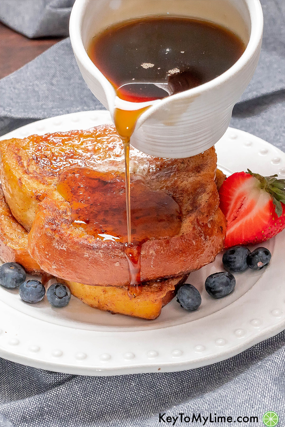 Pouring maple syrup from a small pitcher on top of a stack of French toast.
