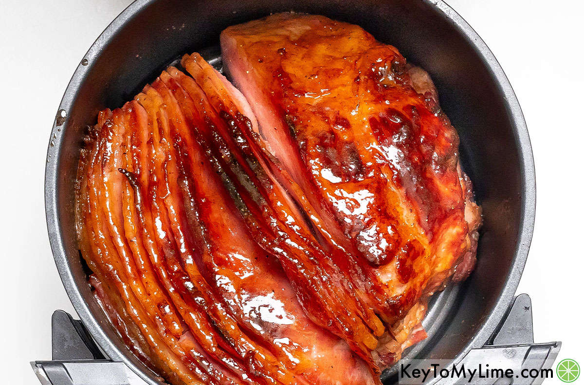 Removing the ham from the air fryer once the glaze has caramelized.