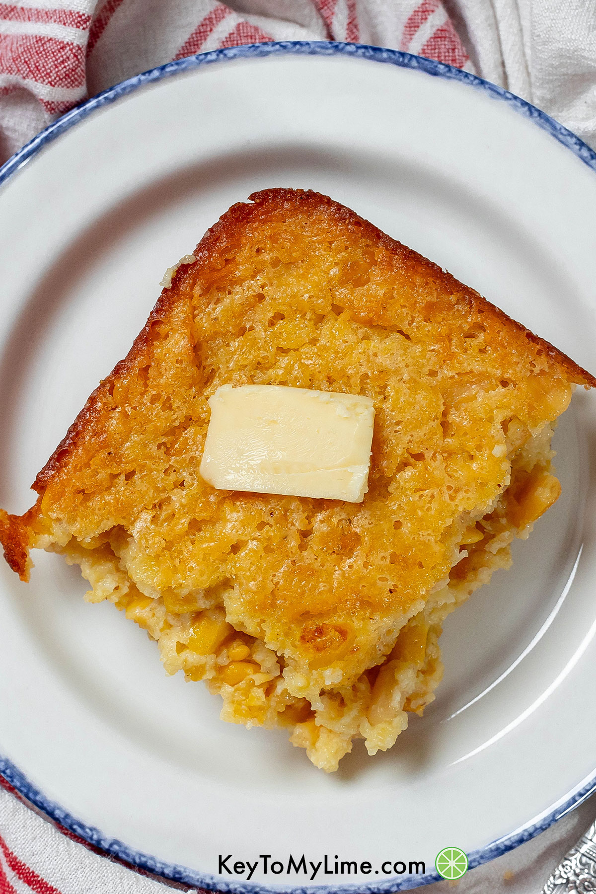 A serving of corn casserole with golden edges and a slab of melted butter on top.
