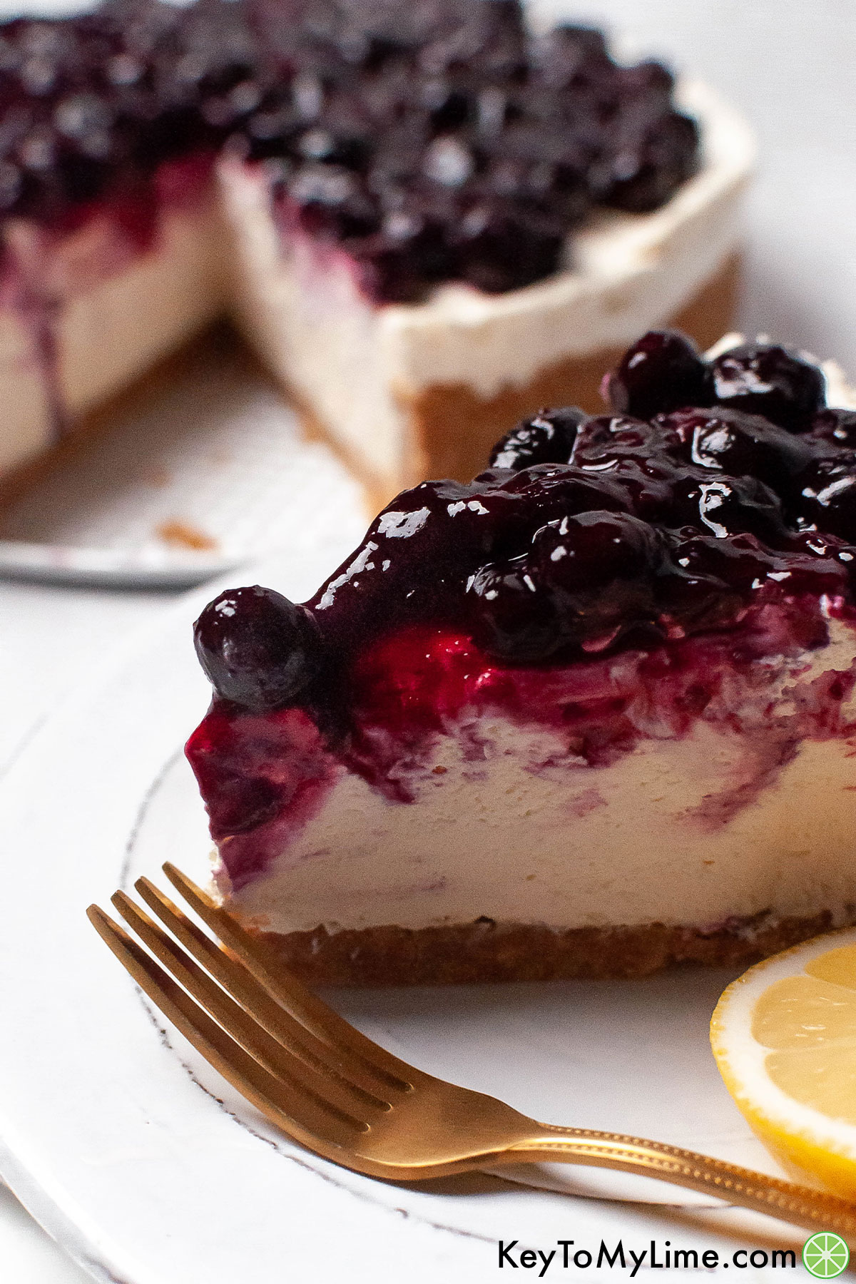 A side image of a slice of cheesecake on top of a white plate garnished with blueberries.