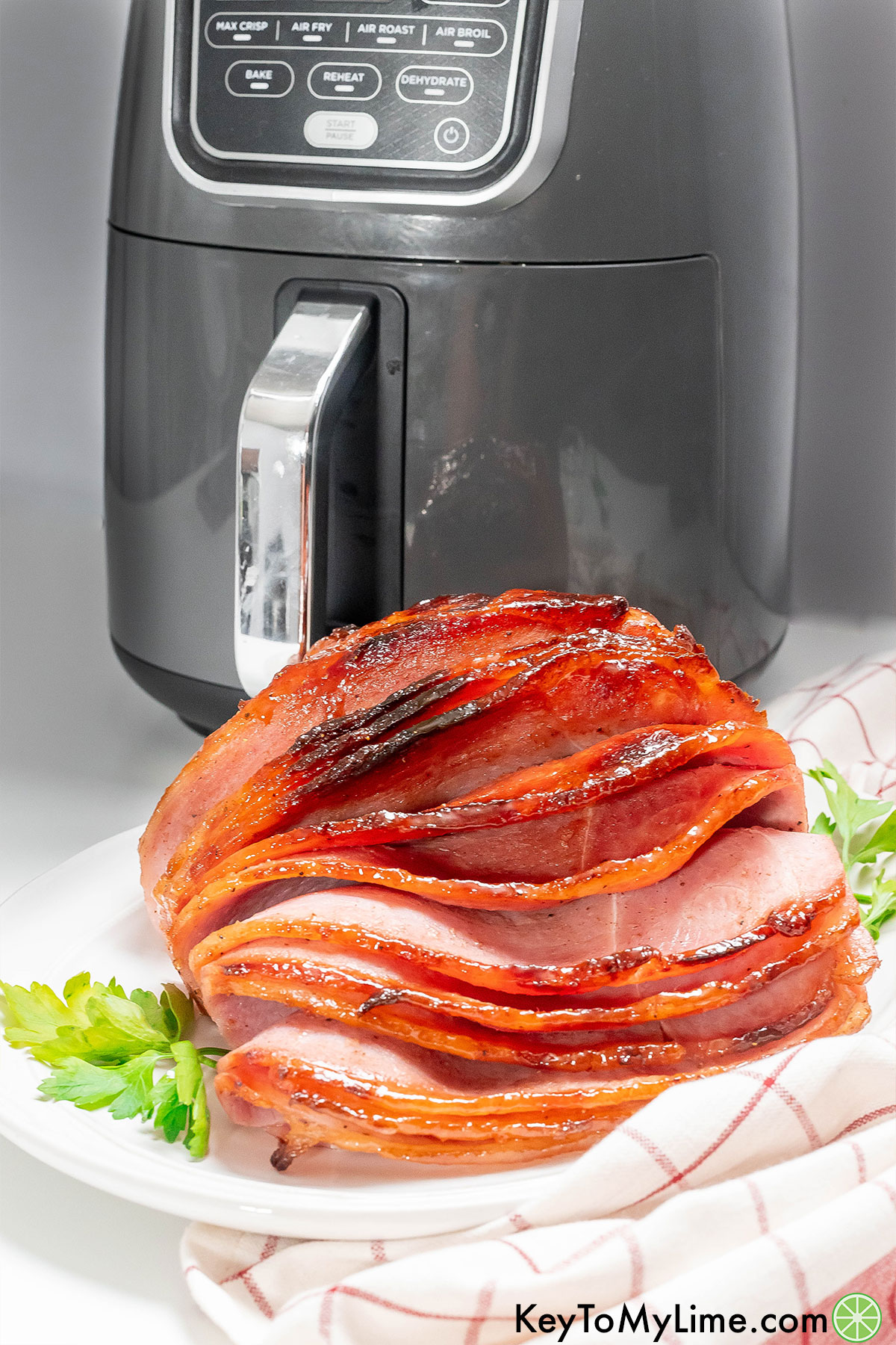 A spiral glazed ham on a large platter in front of an air fryer.