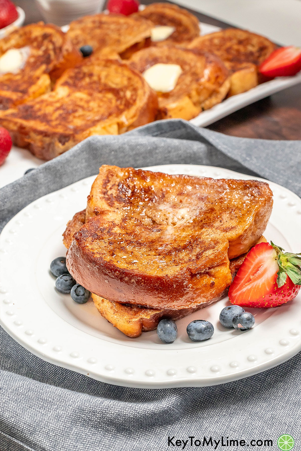A stack of French toast on a white plate with French toast in the background.