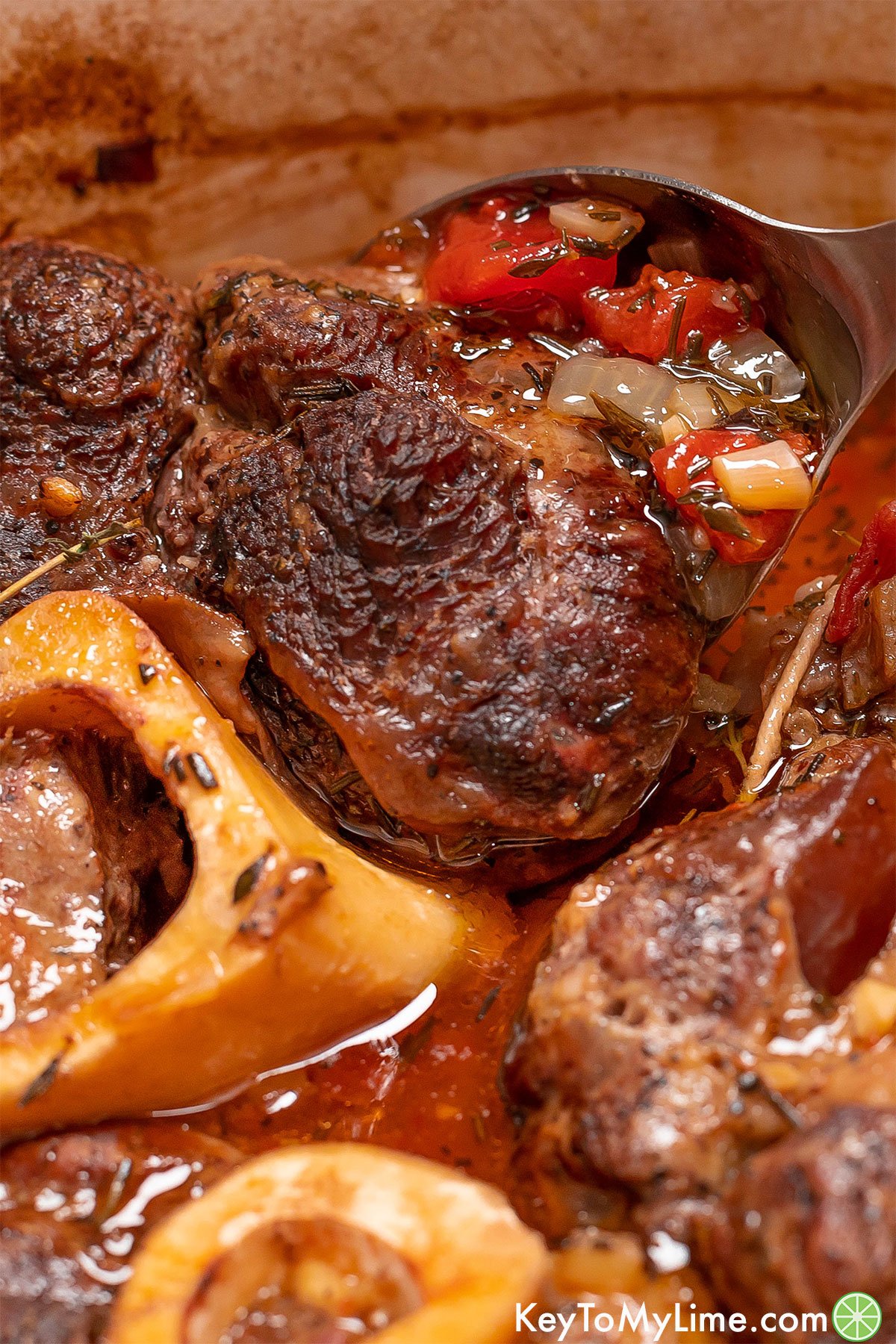 A close up image of a tender fall of the bone beef shank being lifted with a serving spoon.