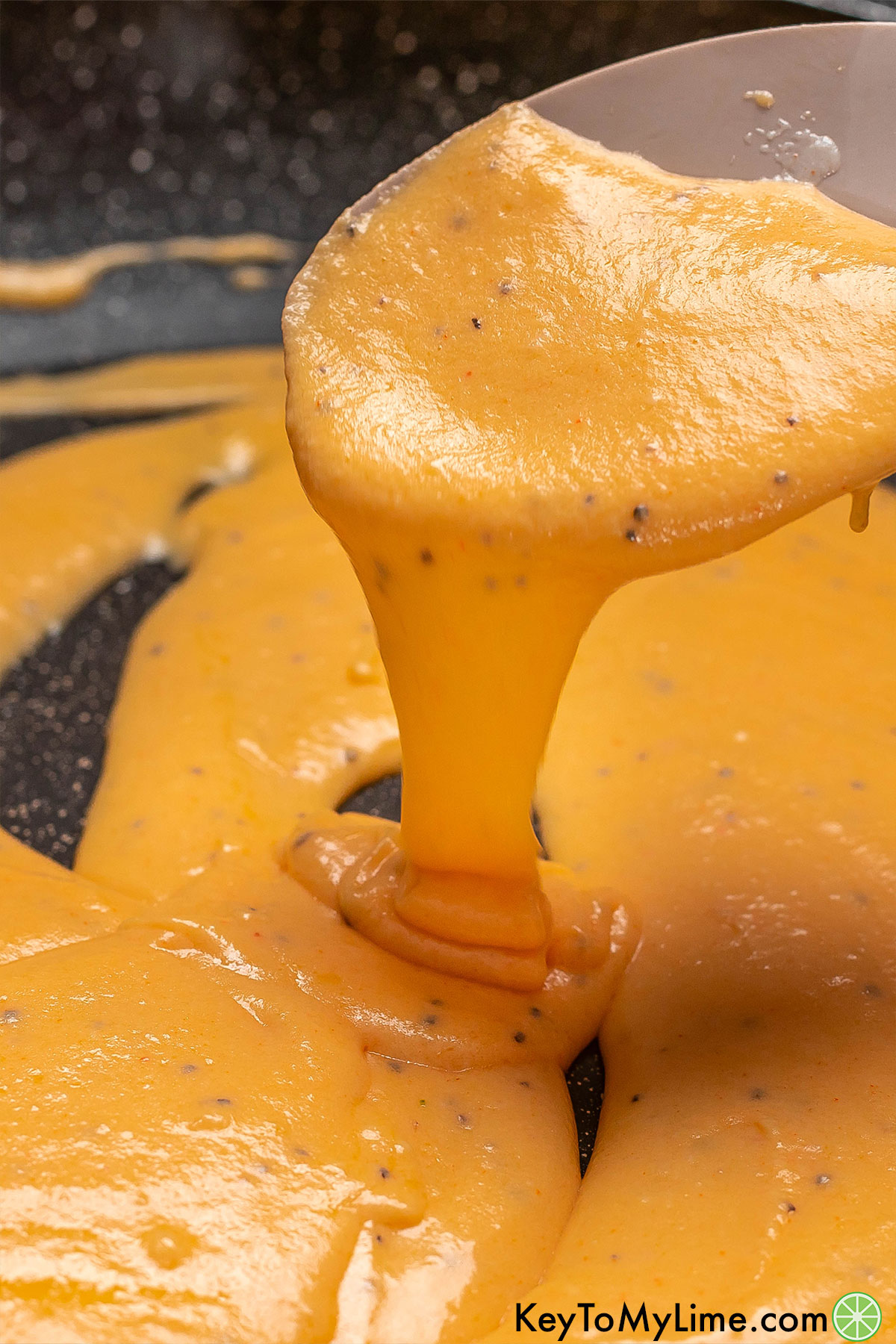 Cheese sauce being lifted out of a hot skillet with a spatula.