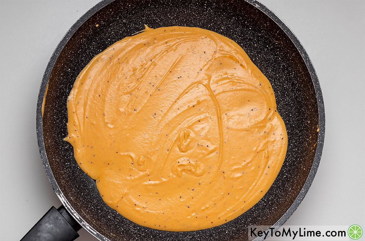 Mixing salt and pepper into the cheese sauce in a hot skillet.