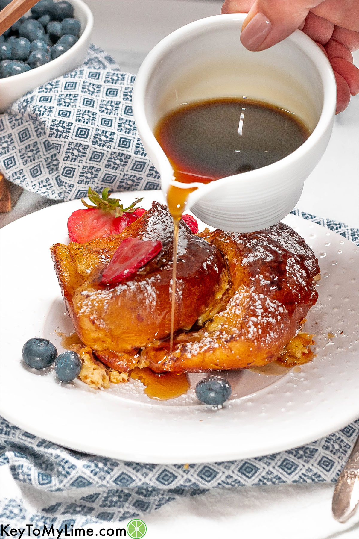 A slice of French toast on a white plate with maple syrup being poured over top.