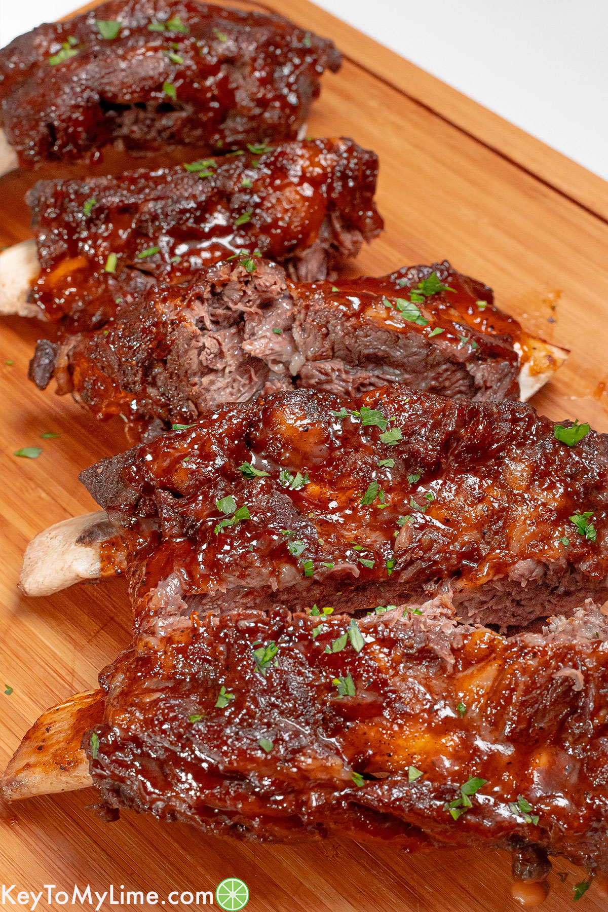 A side image of fully cooked beef ribs garnished with fresh parsley on top.