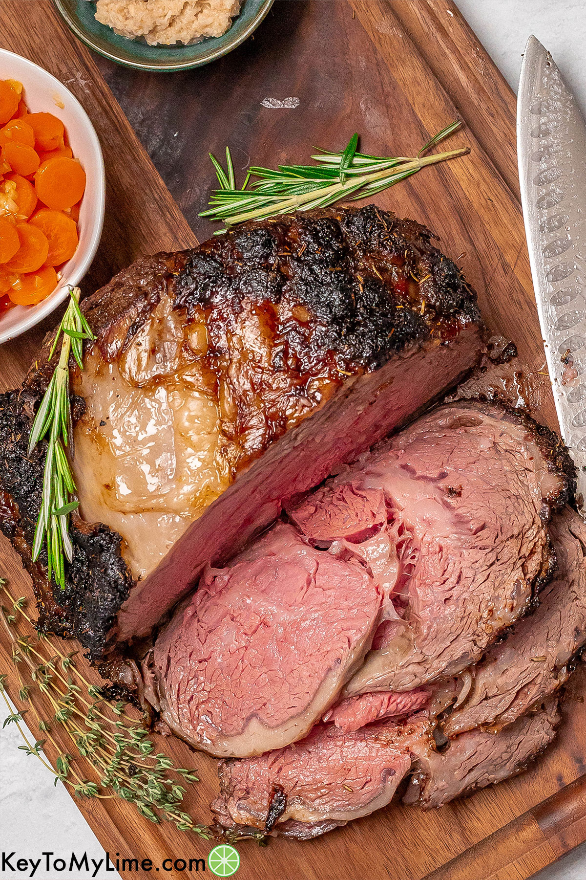An overhead image of a sliced beef roast with horseradish and carrots to the side.