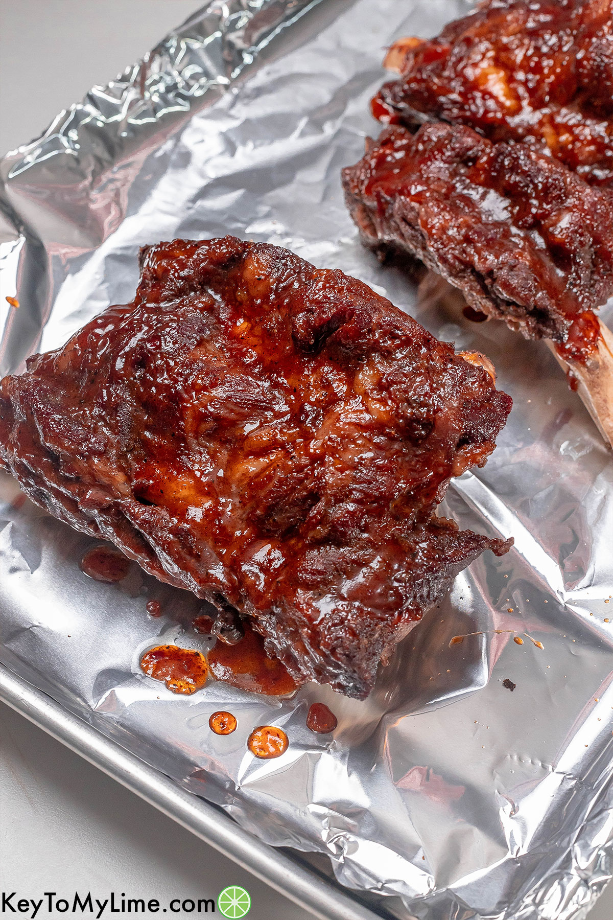 A side image of a couple of broiled ribs fresh out of the oven on a lined baking sheet.