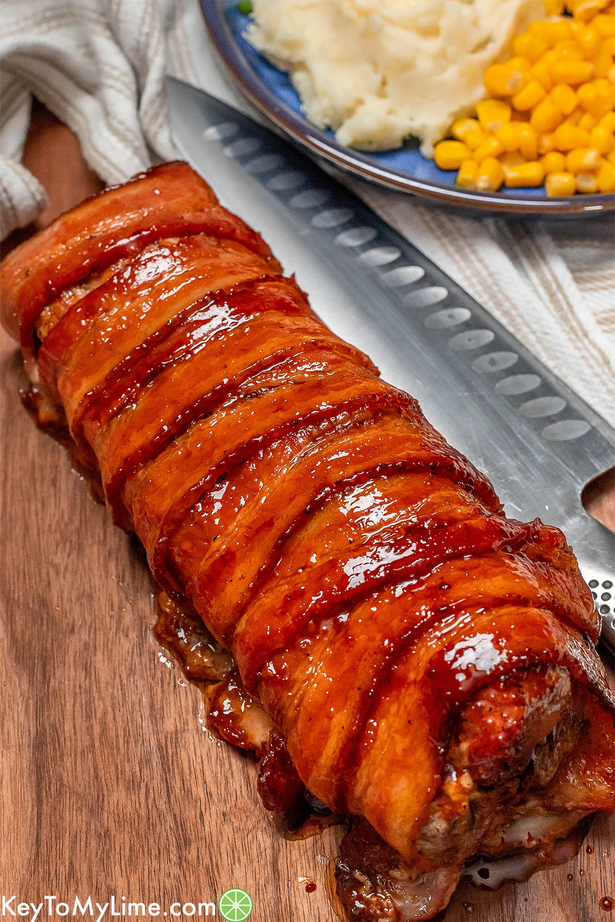 An angled image of a beautifully cooked bacon wrapped tenderloin with glaze on top.