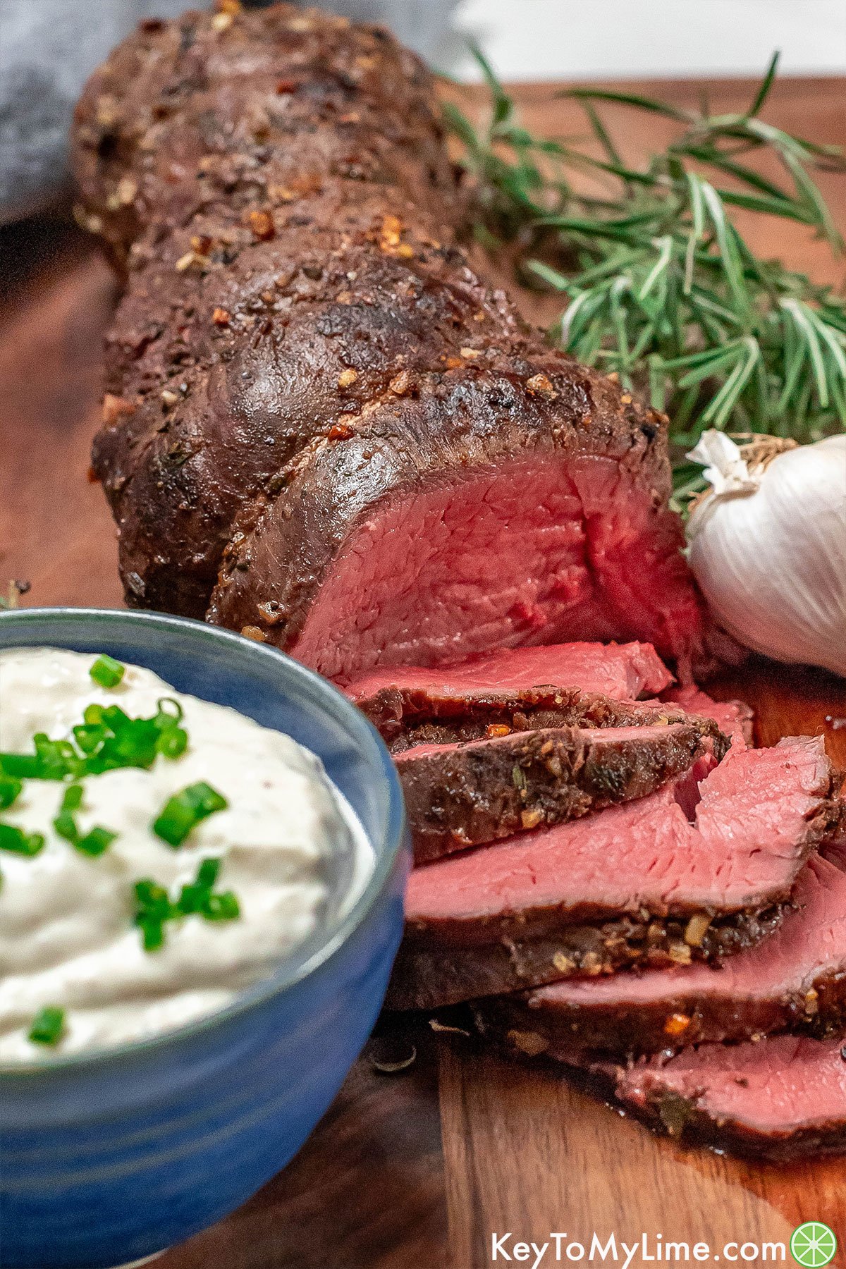 A partially sliced beef tenderloin resting on a cutting board next to a small bowl of horseradish sauce.