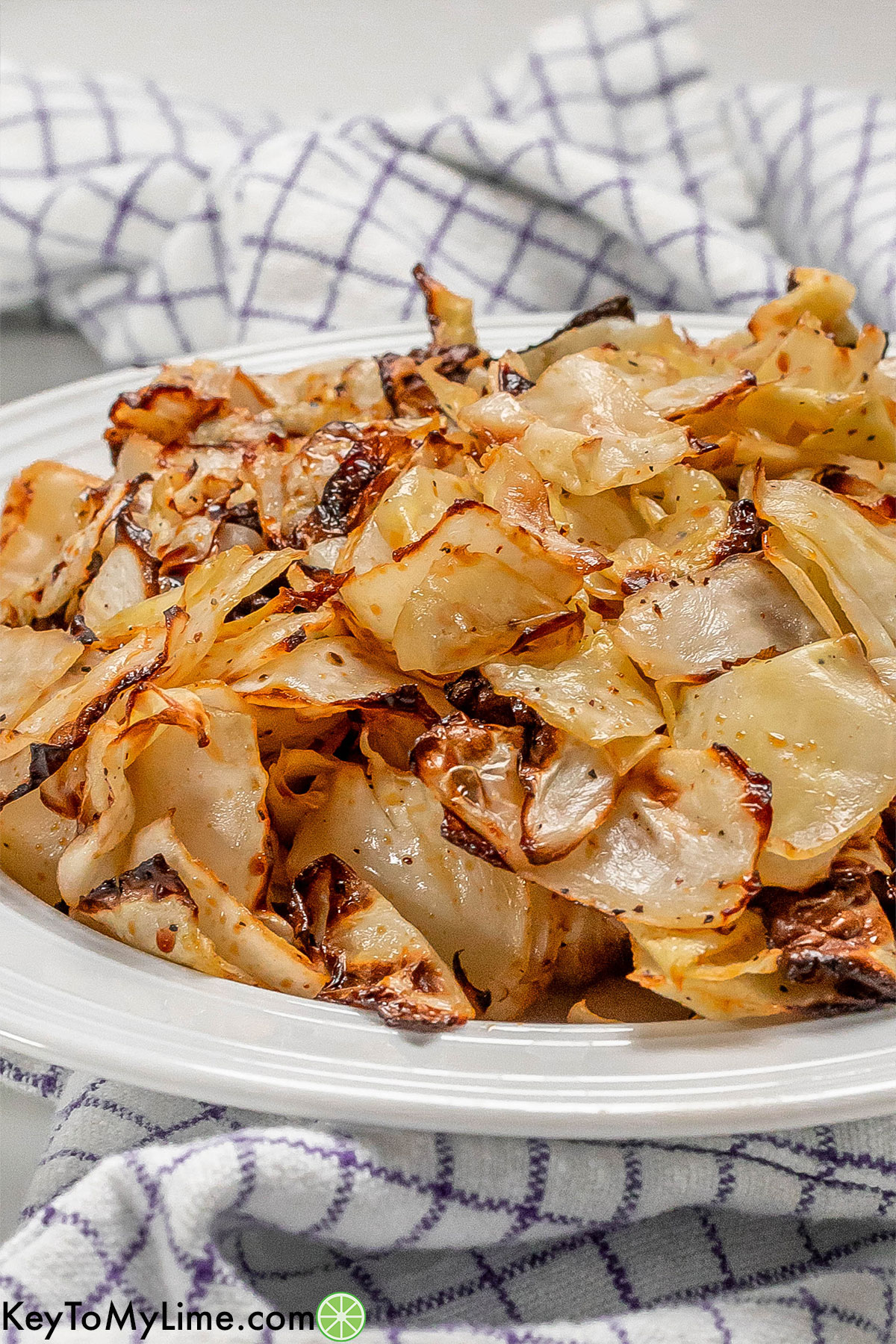A side image of air fried cabbage piled up in a white bowl with a striped napkin underneath.