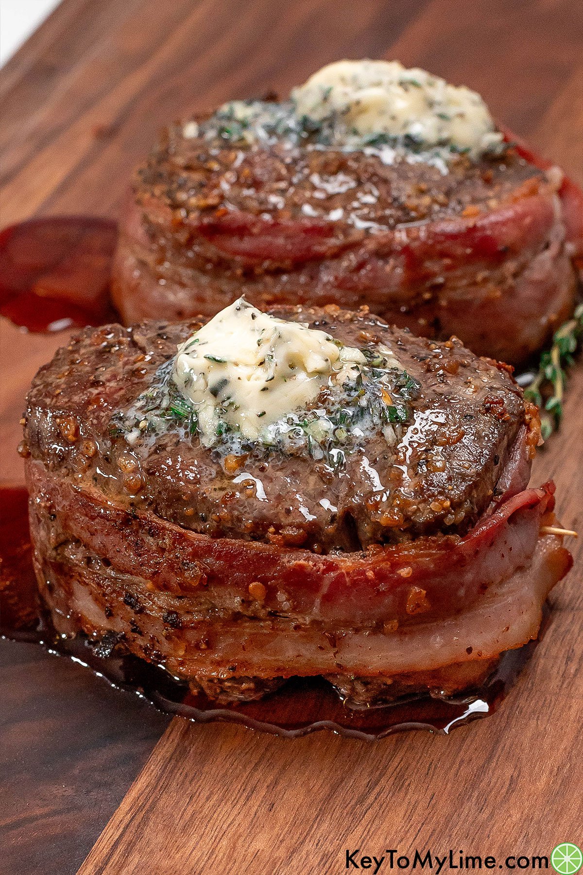 A side image showing the melted butter on top of the pair of cooked filet mignons resting on a cutting board.