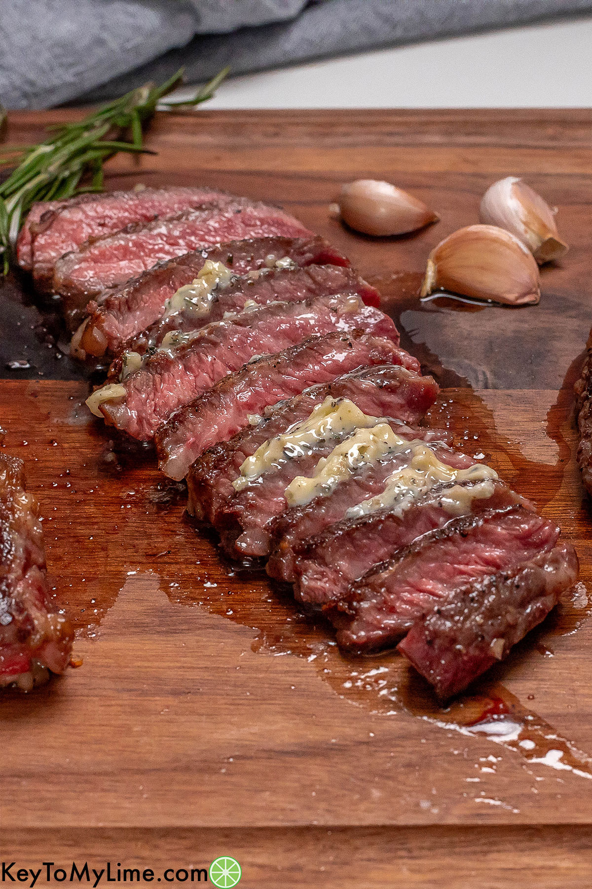 An angled image of sliced steak resting on a cutting board with garlic to the side.