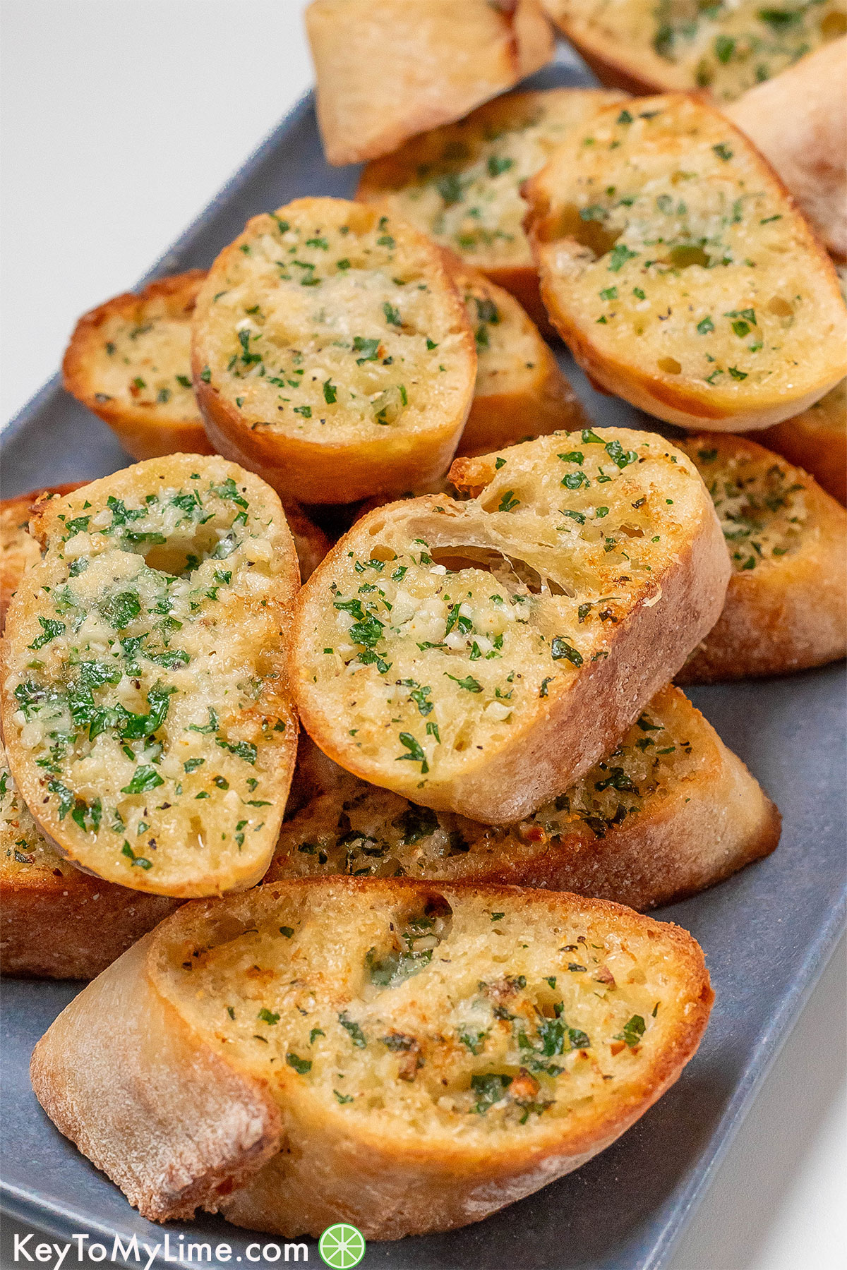 A side image of freshly cooked garlic bread spread on a platter with herbs and garlic throughout.