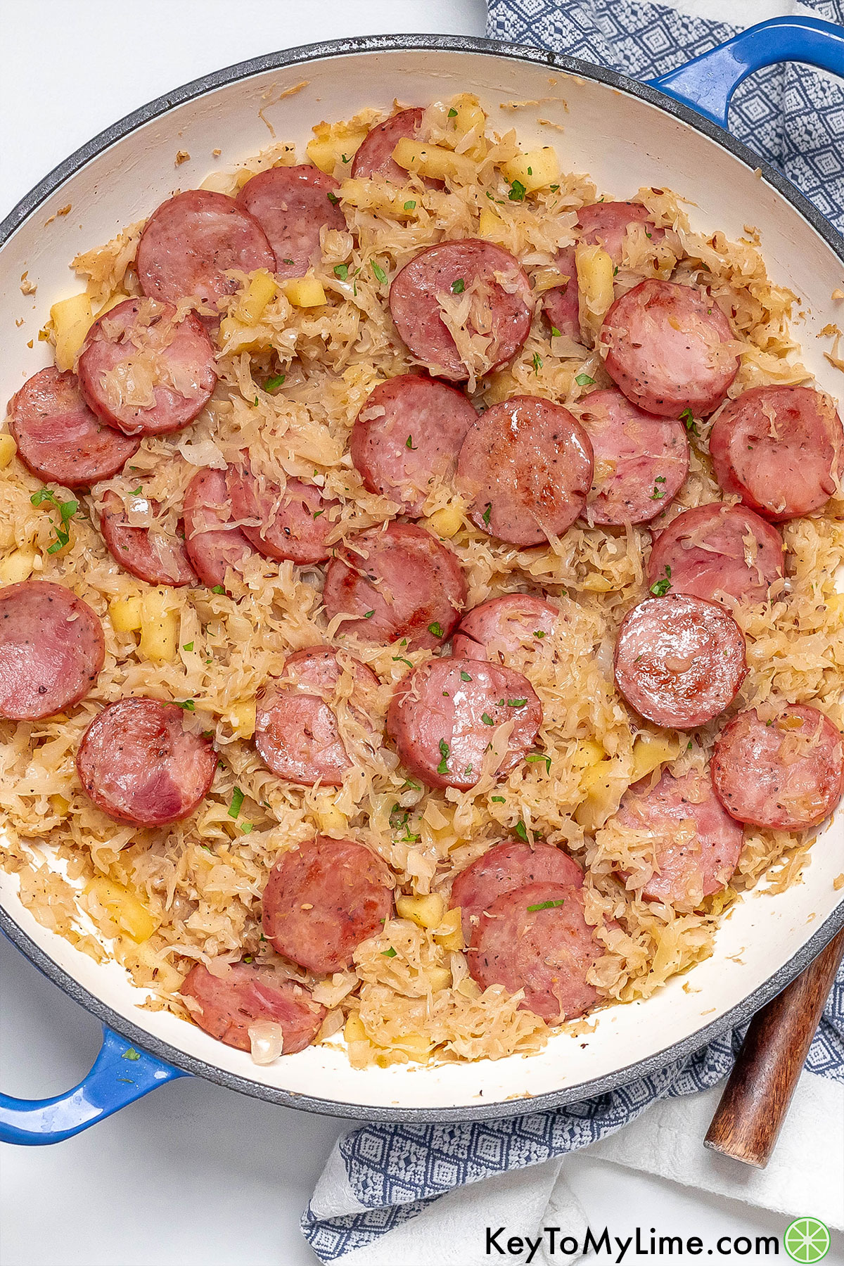An overhead image of a large skillet filled with fully cooked kielbasa sausage and sauerkraut.