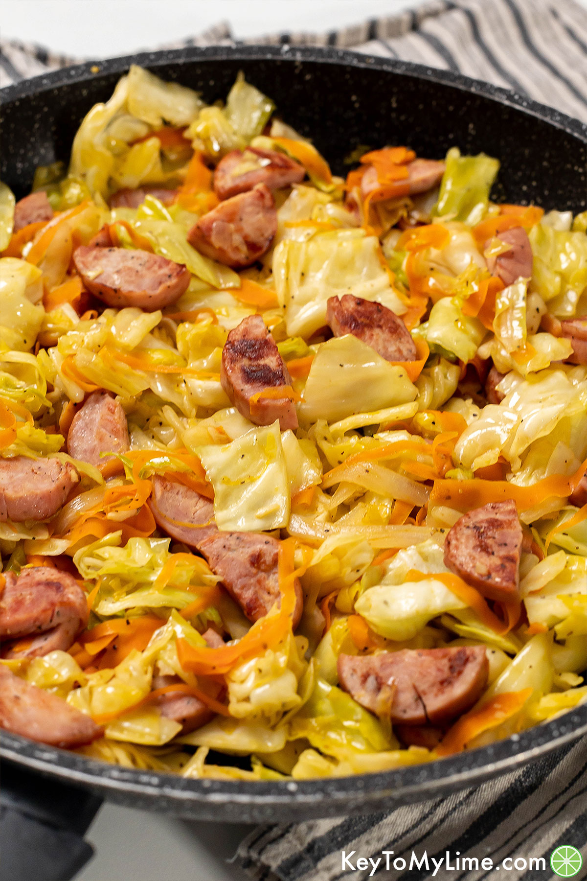 A fully cooked cabbage and sausage meal in a large skillet.