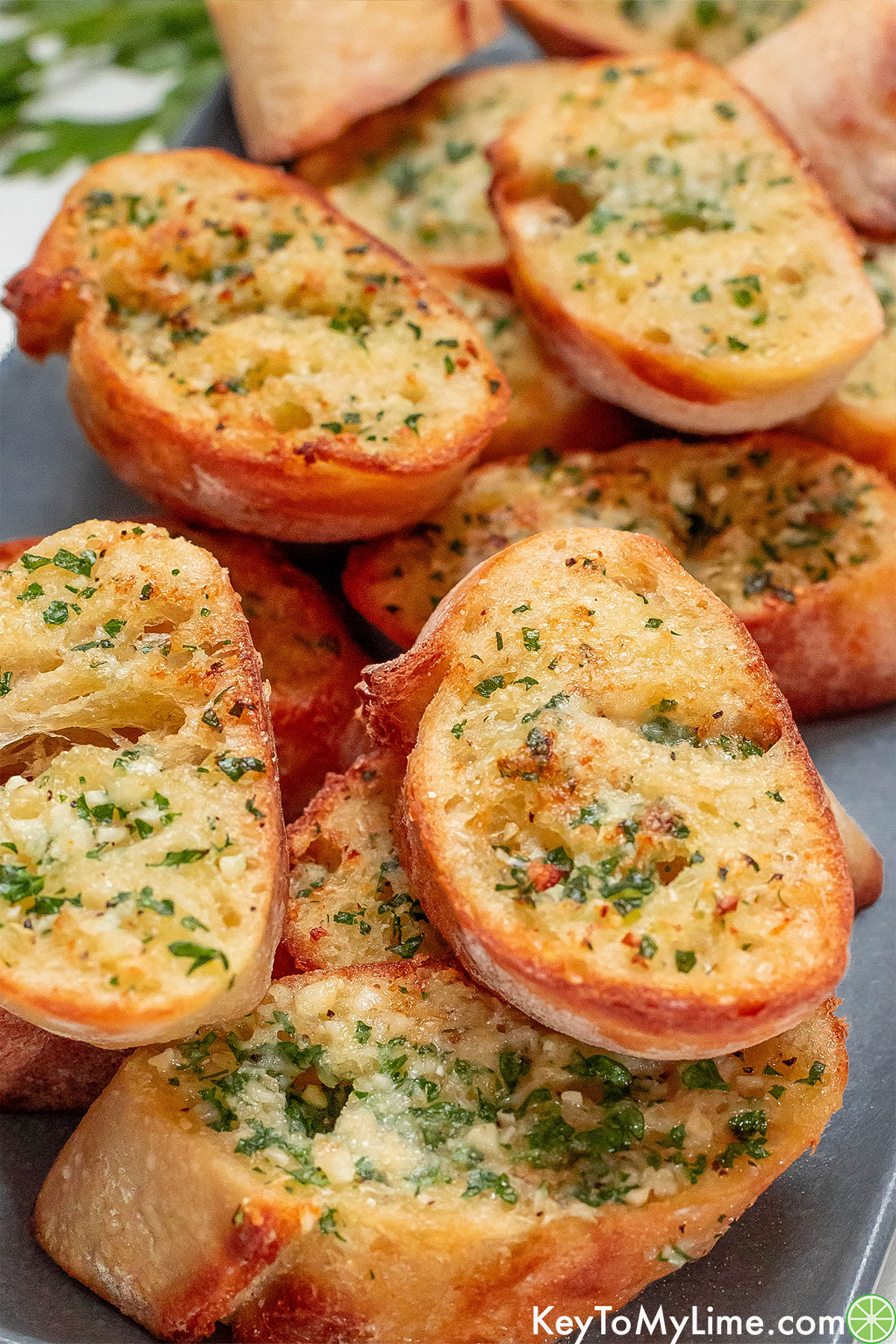 A close up image showing crispy garlic bread glistening with butter and fresh herbs.