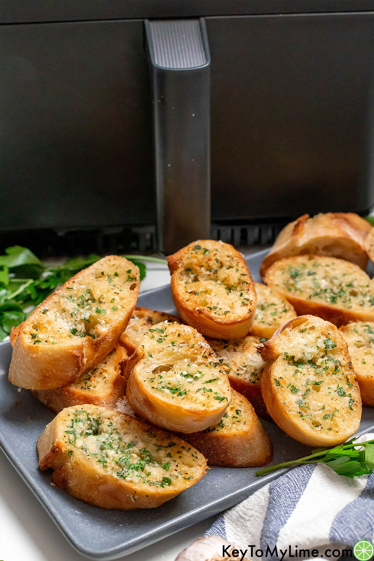 A side image of garlic bread on a platter with an air fryer in the background.